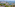 Aerial view of a beachfront resort with pools, palm trees, ocean, and mountains.