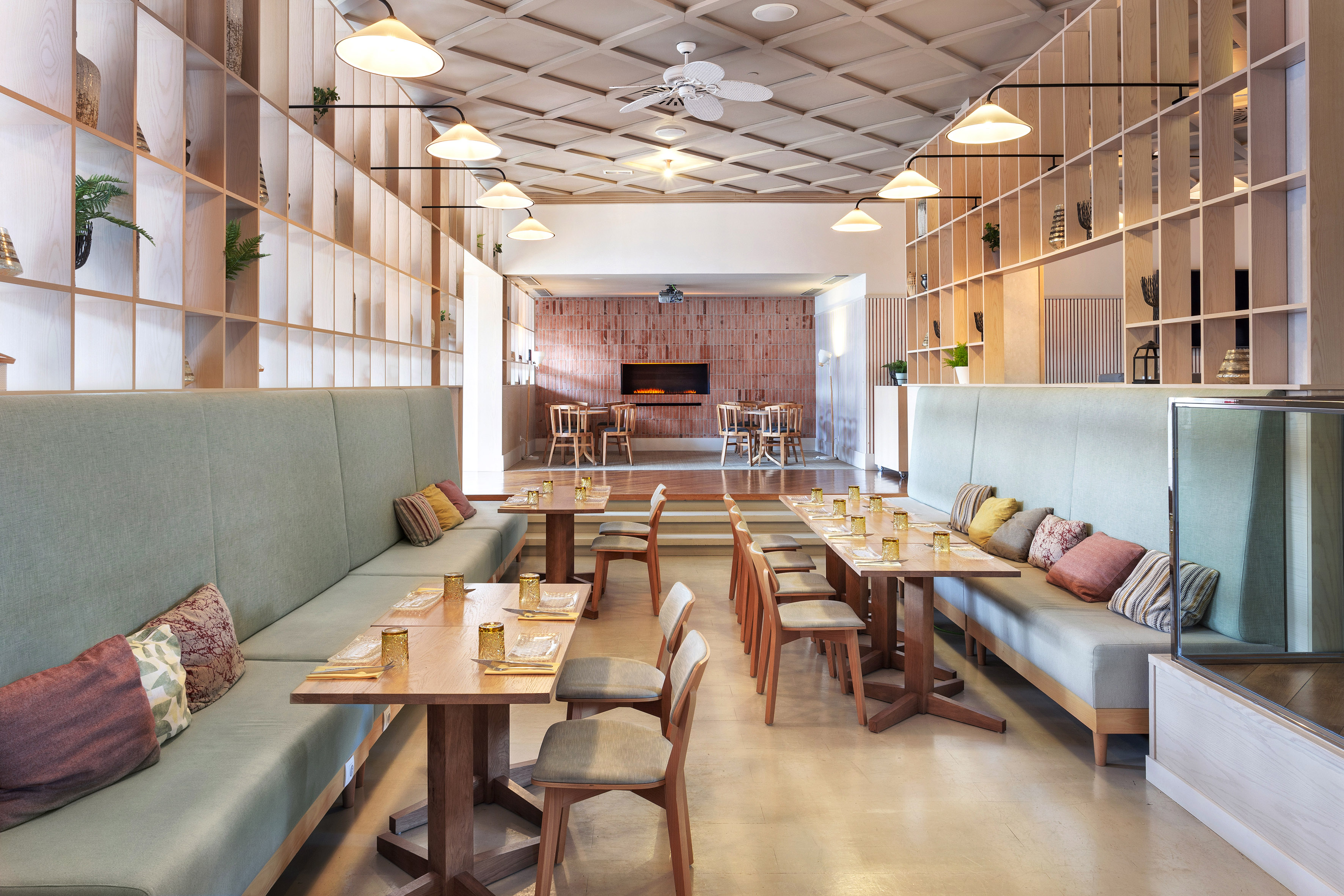 Modern restaurant dining room with green banquettes, wood tables, and light shelving.