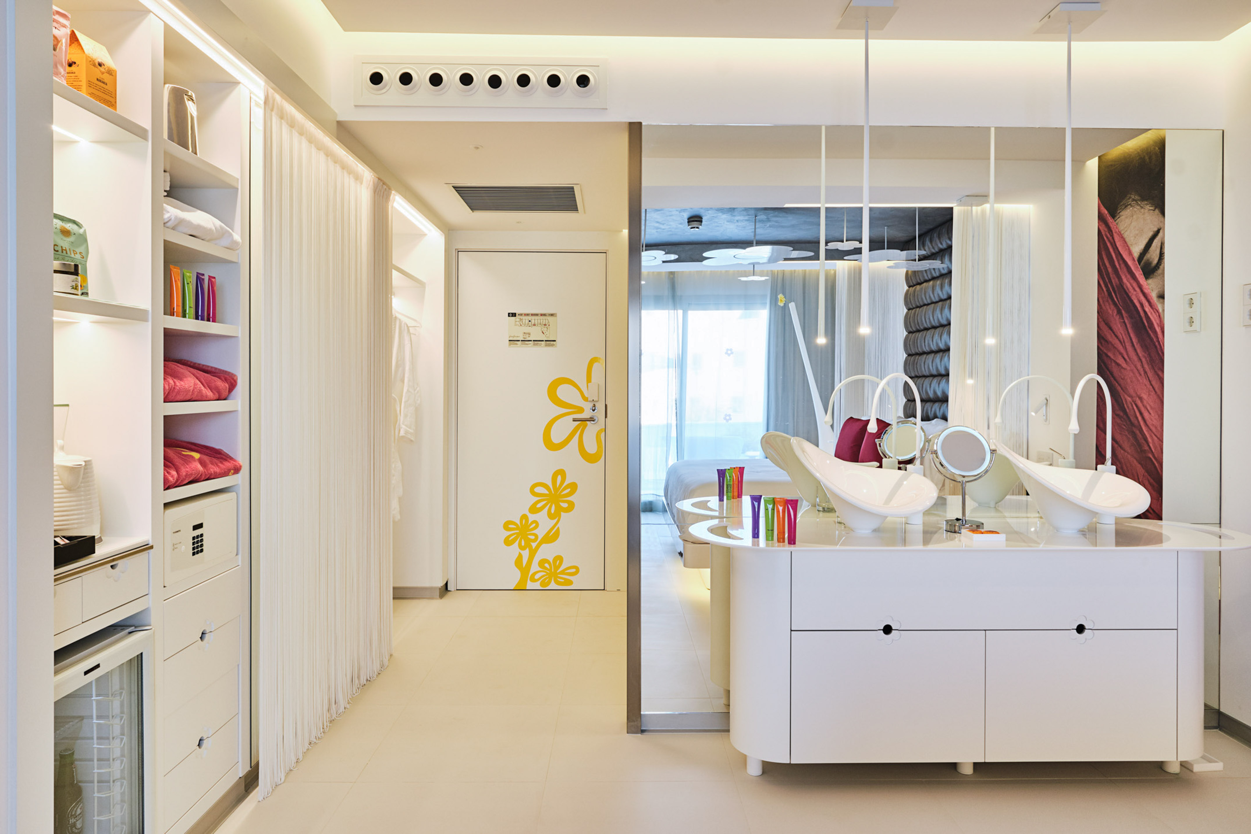 Modern hotel room: white storage, floral door, and sleek dual-sink vanity.