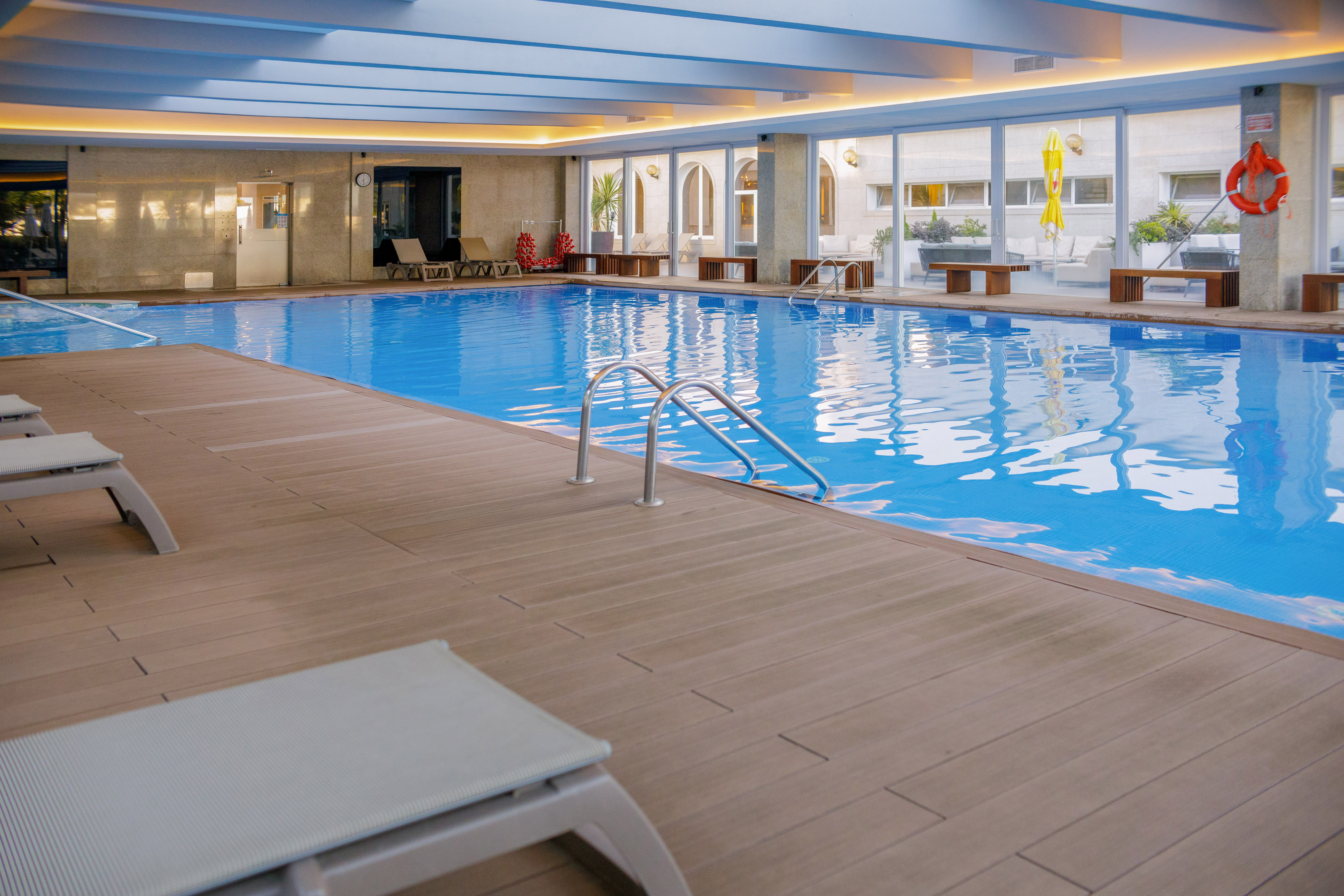 Modern indoor hotel pool with blue water, wooden deck, and sun loungers.