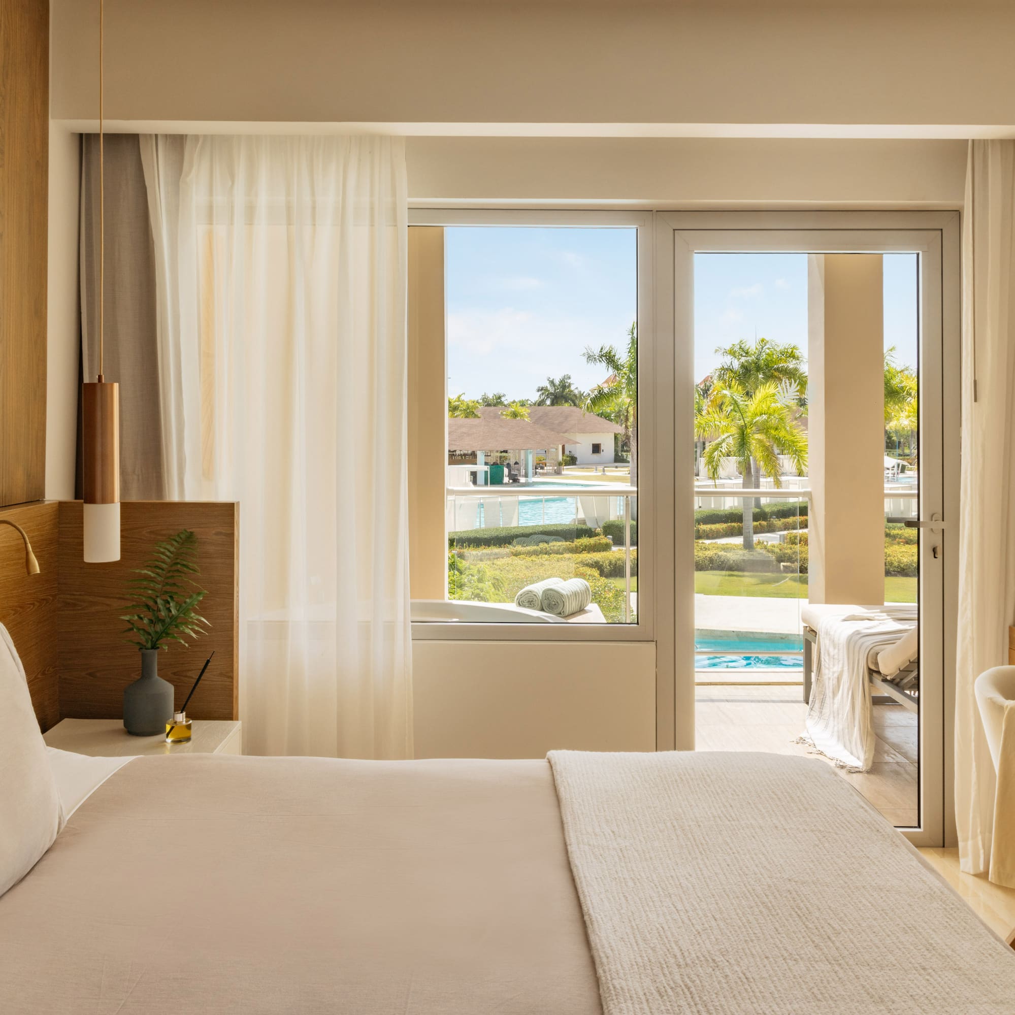 Luxurious resort bedroom with king bed, balcony, and tropical pool view.