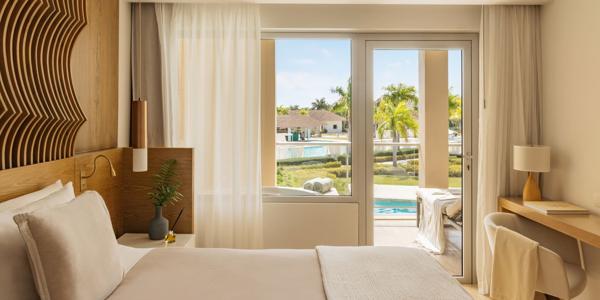 Luxurious resort bedroom with king bed, balcony, and tropical pool view.