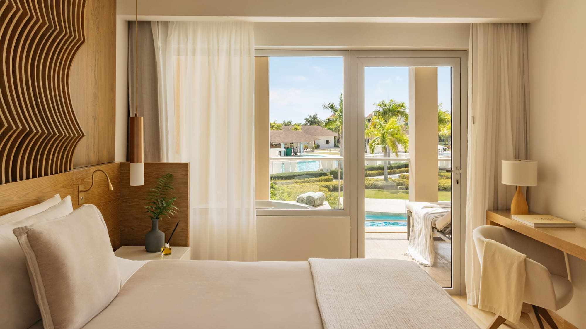 Luxurious resort bedroom with king bed, balcony, and tropical pool view.