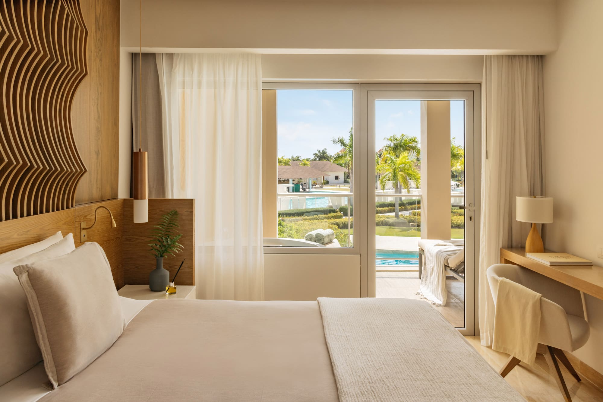 Luxurious resort bedroom with king bed, balcony, and tropical pool view.