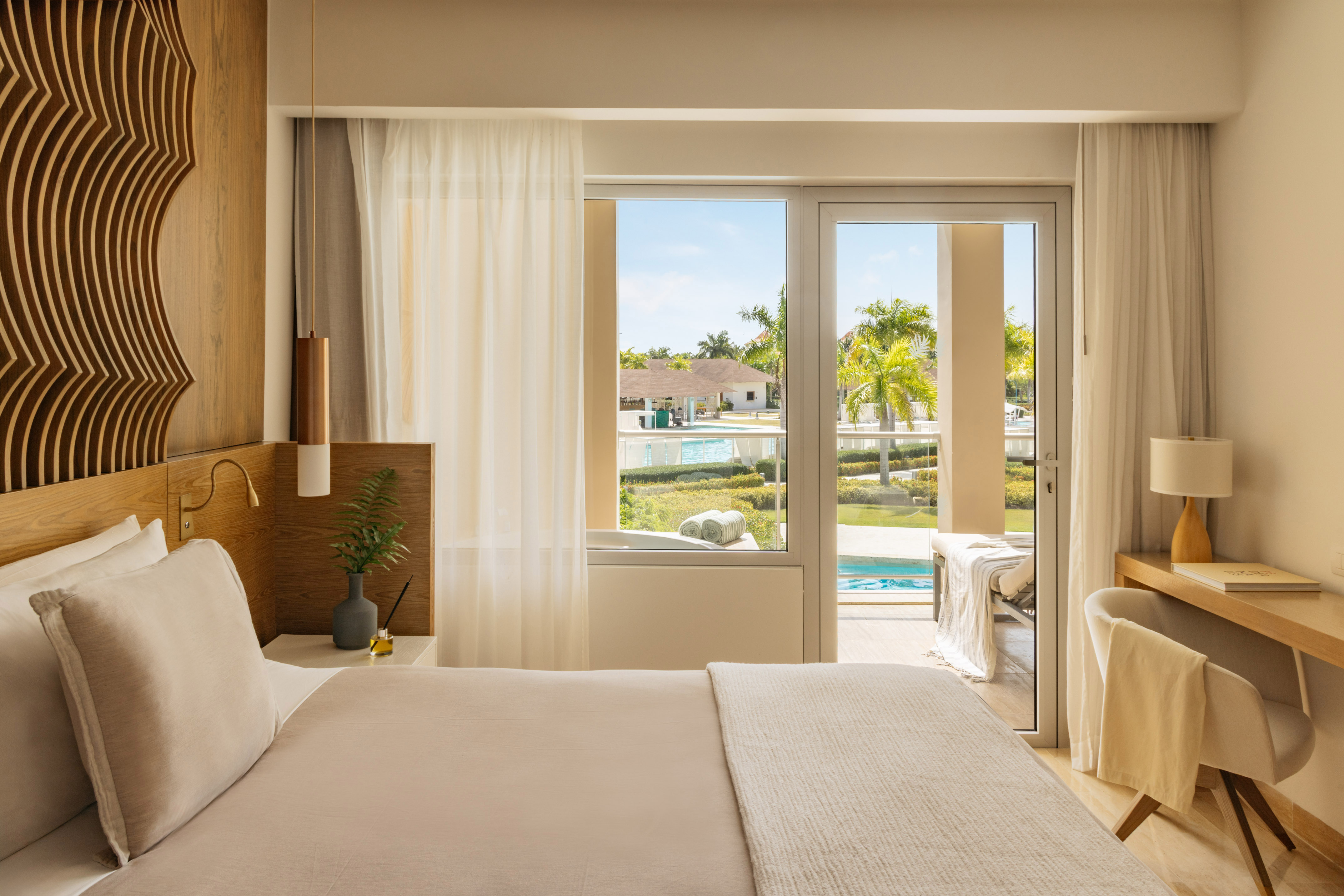 Luxurious resort bedroom with king bed, balcony, and tropical pool view.