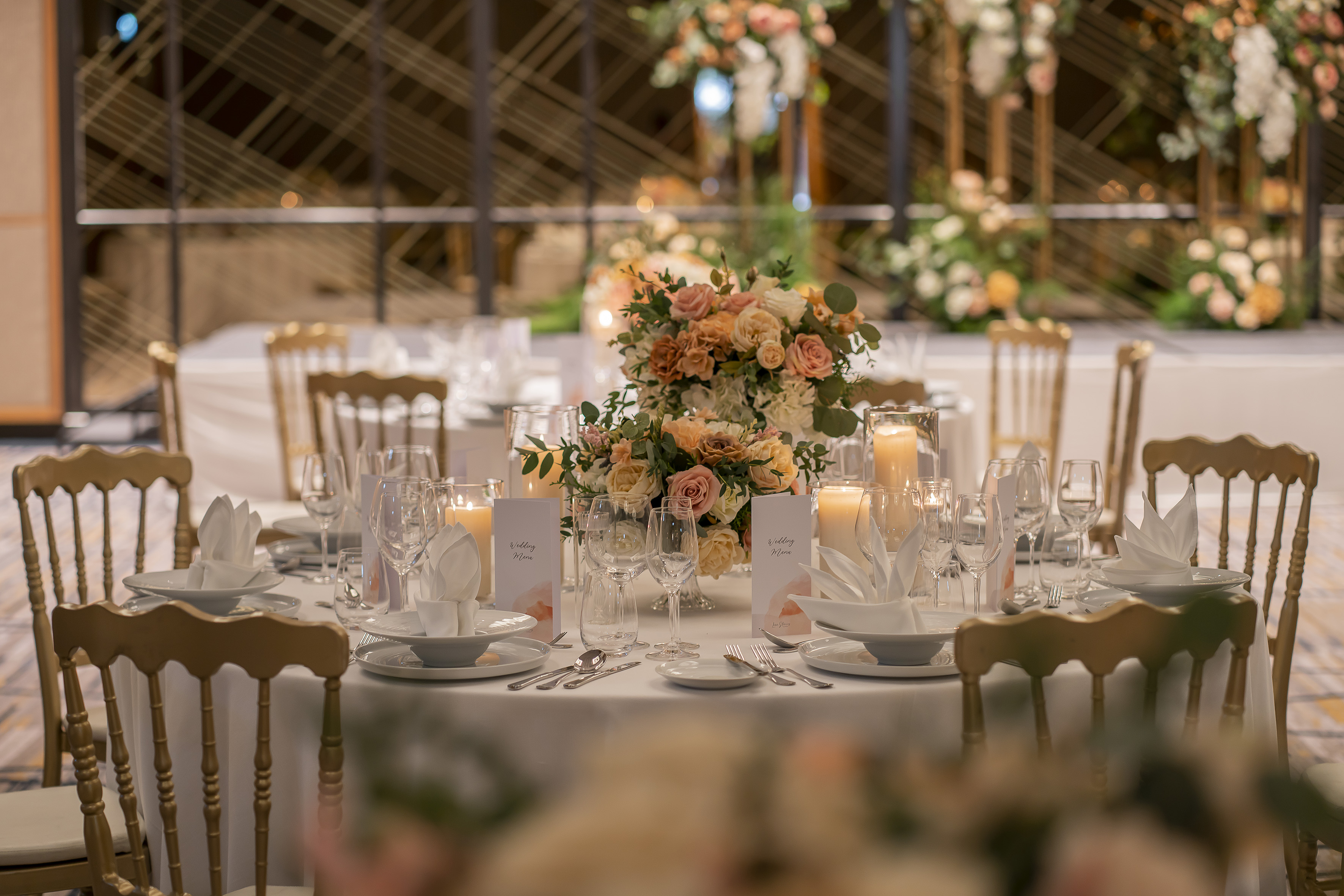 Wedding reception table set with peach florals, candles, and gold chairs.