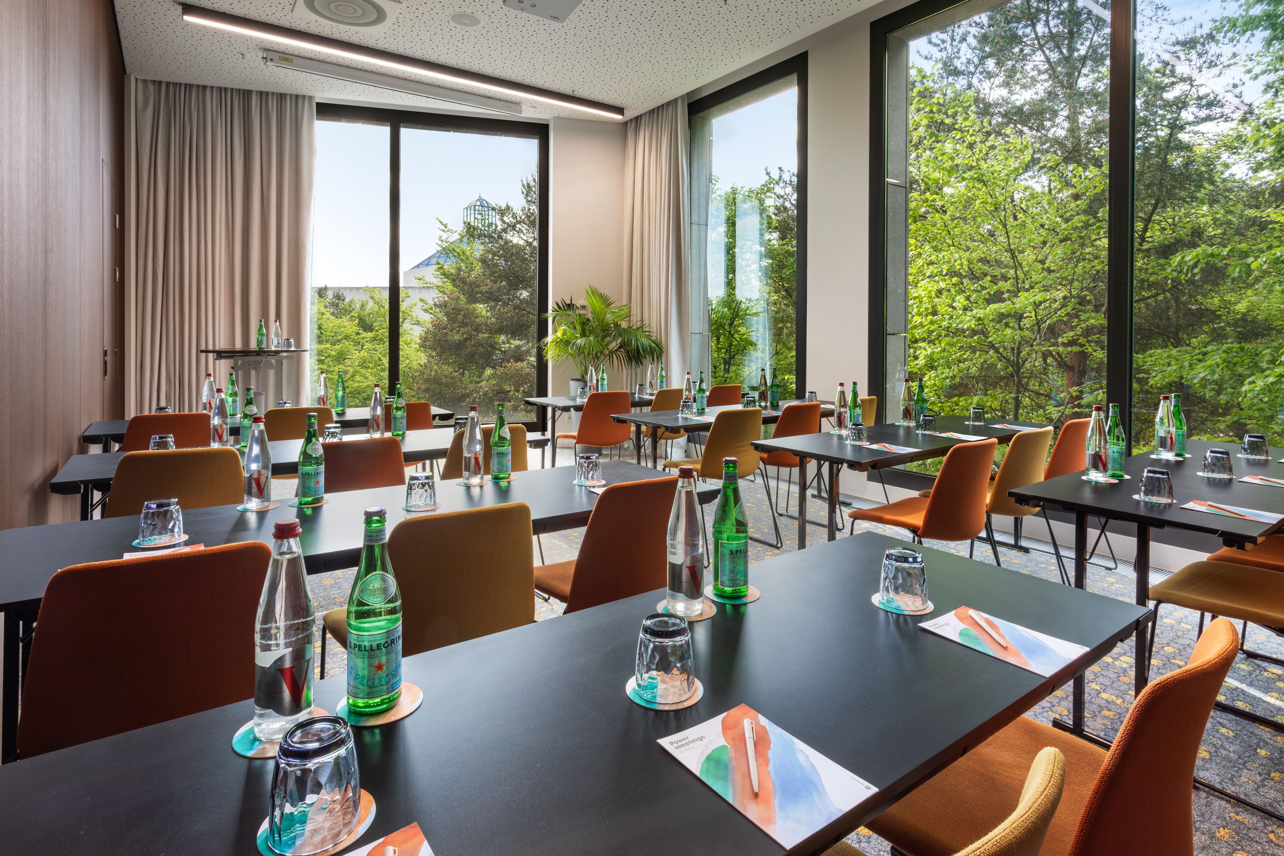 Modern meeting room with large windows, nature view, tables, and chairs.