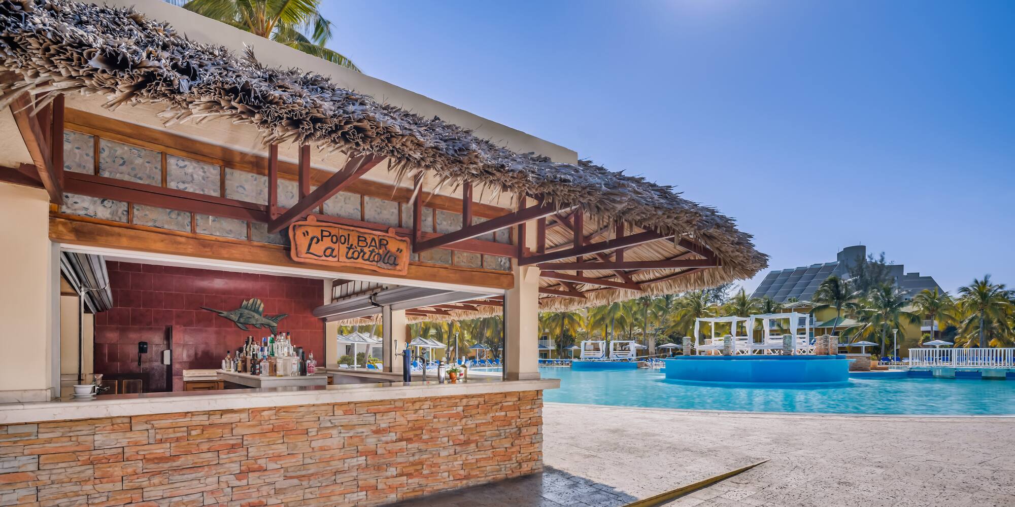 a bar with a straw roof next to a pool