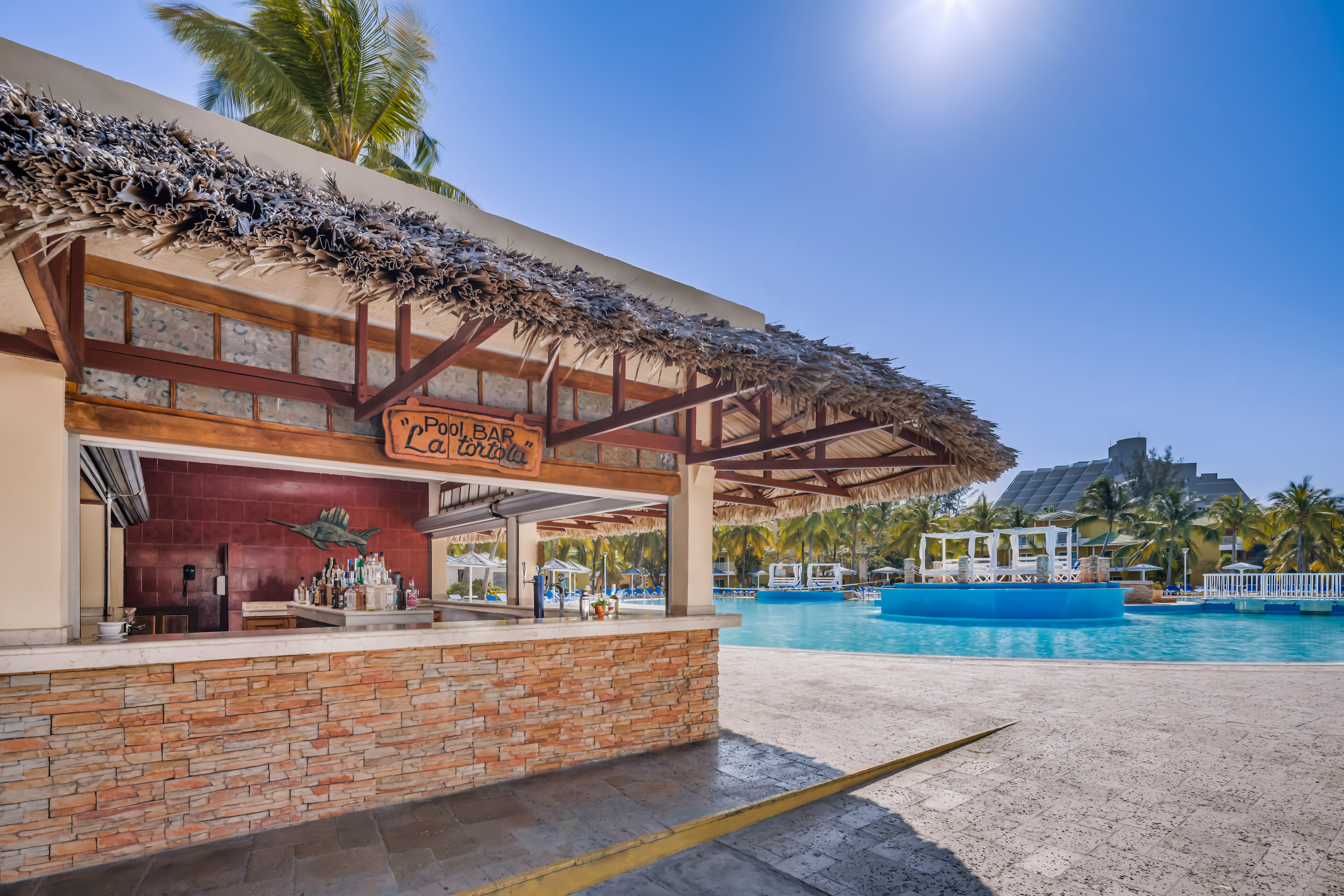 a bar with a straw roof next to a pool