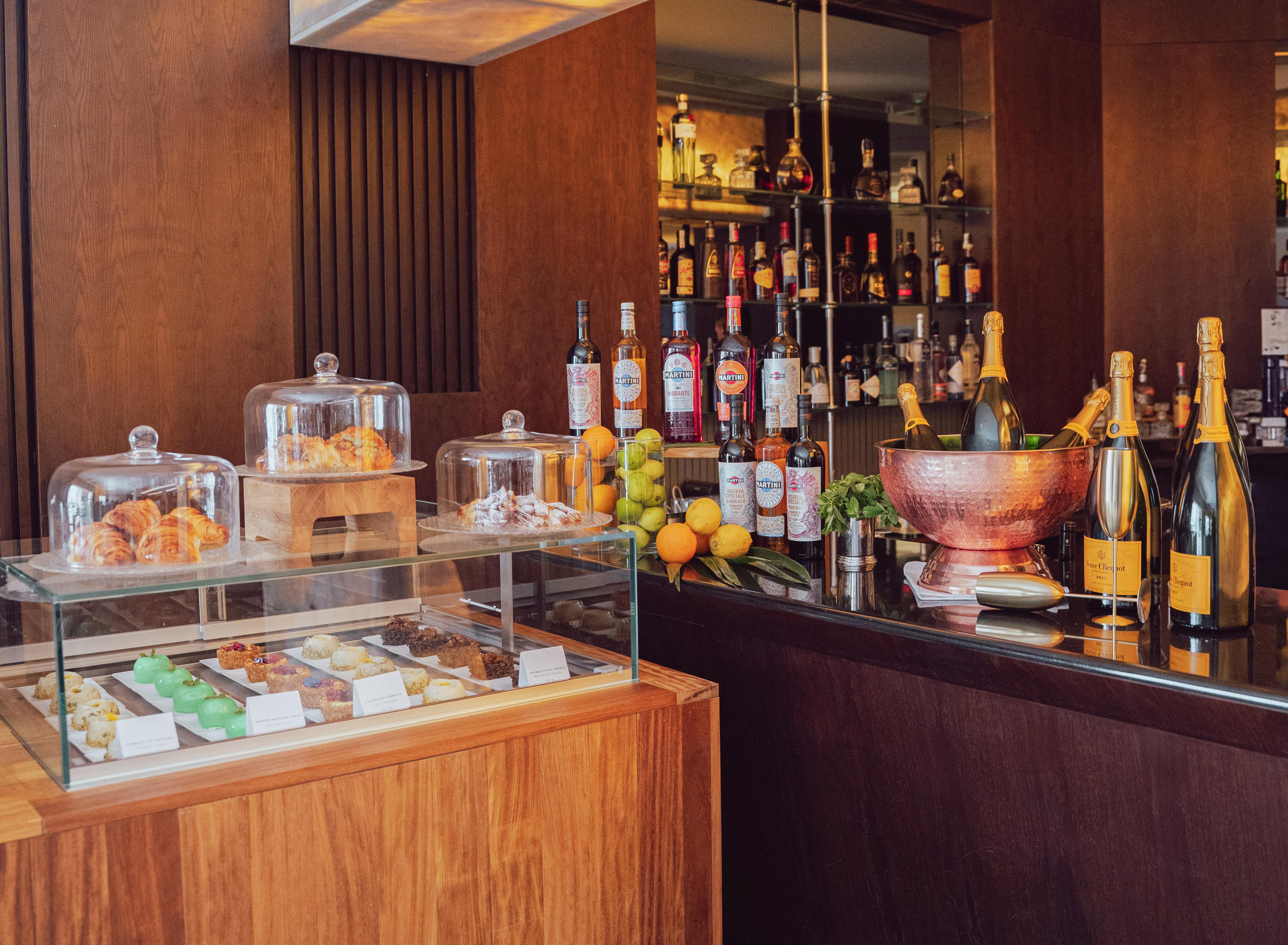 Hotel bar counter with pastries, desserts, champagne, and cocktail bottles.