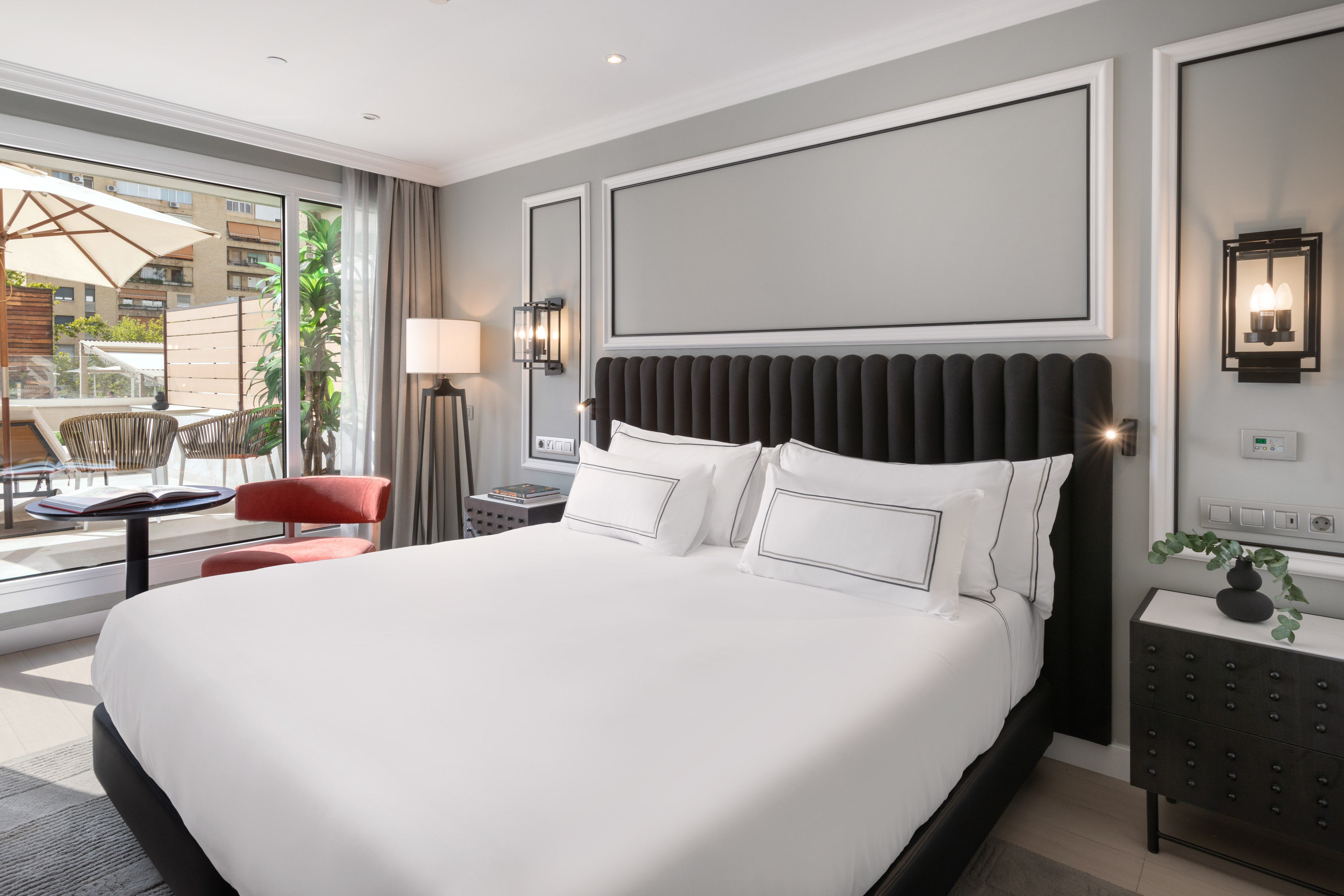 Contemporary hotel bedroom with white bed, black headboard, and balcony.