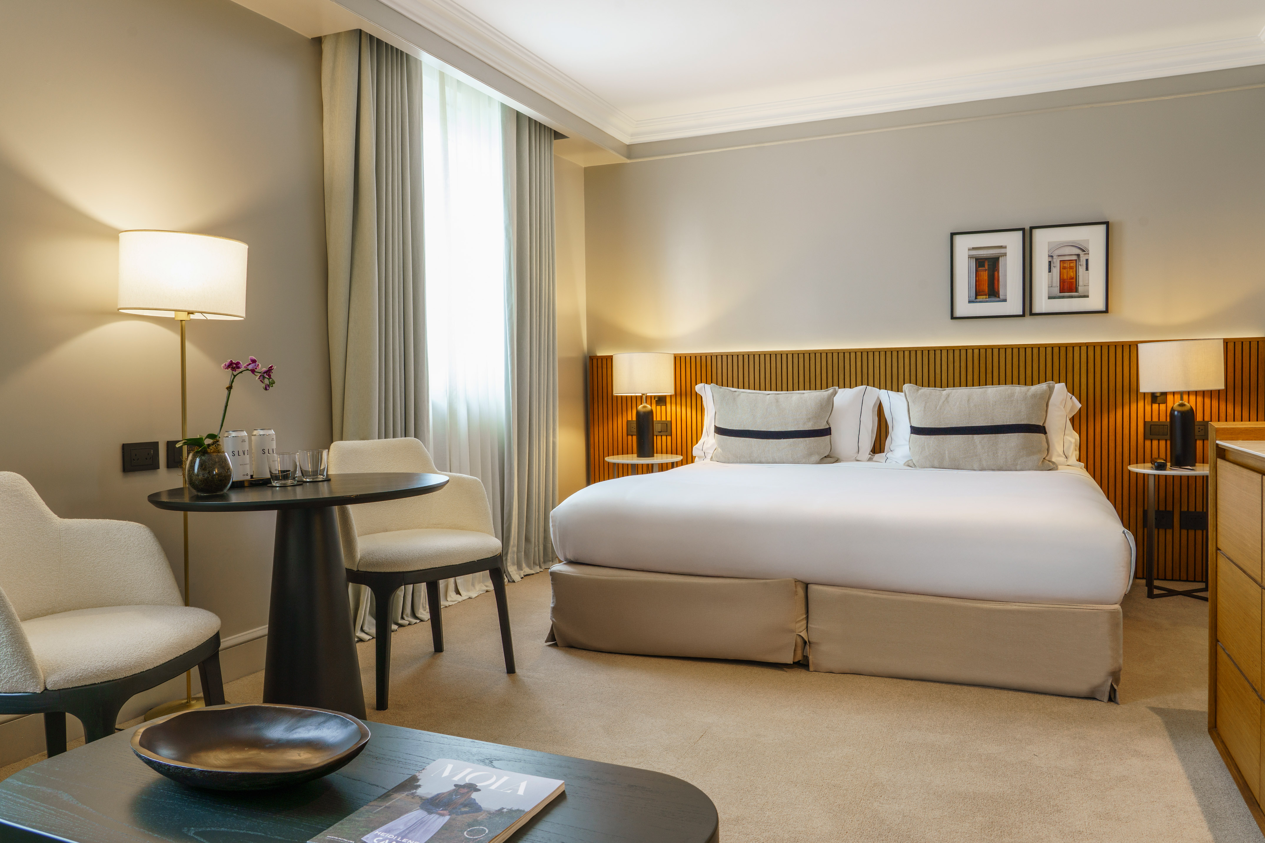 Luxury hotel bedroom with large bed, wooden headboard, and seating area.