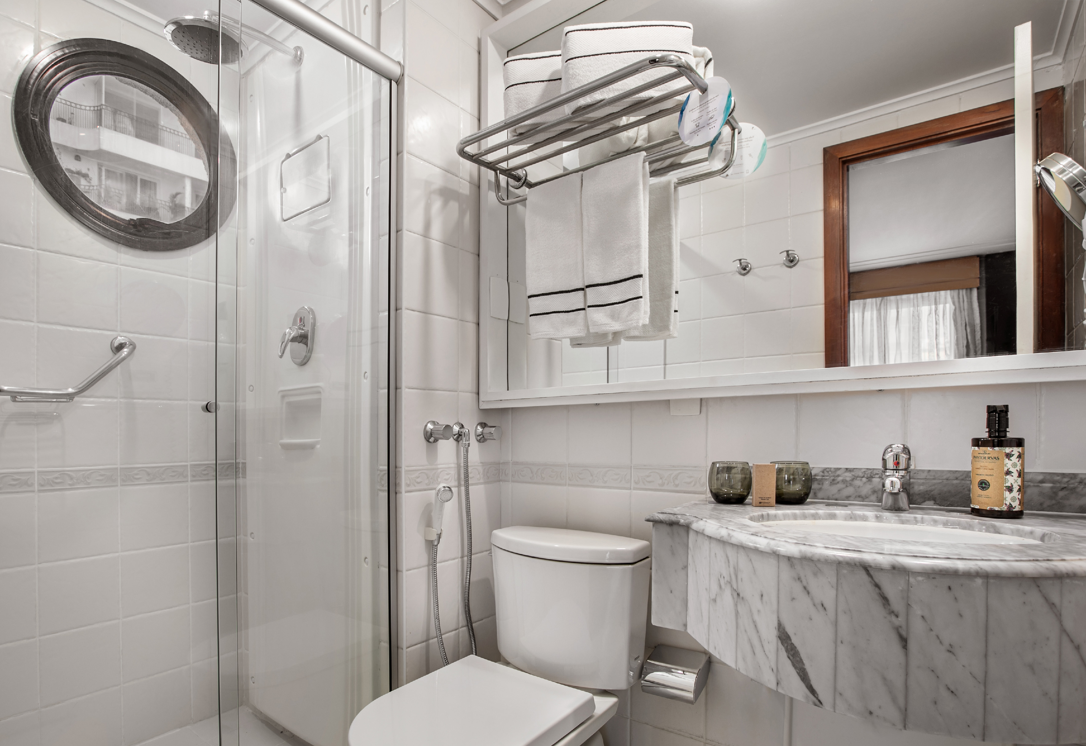 White tiled hotel bathroom with shower, toilet, marble vanity, and fresh towels.