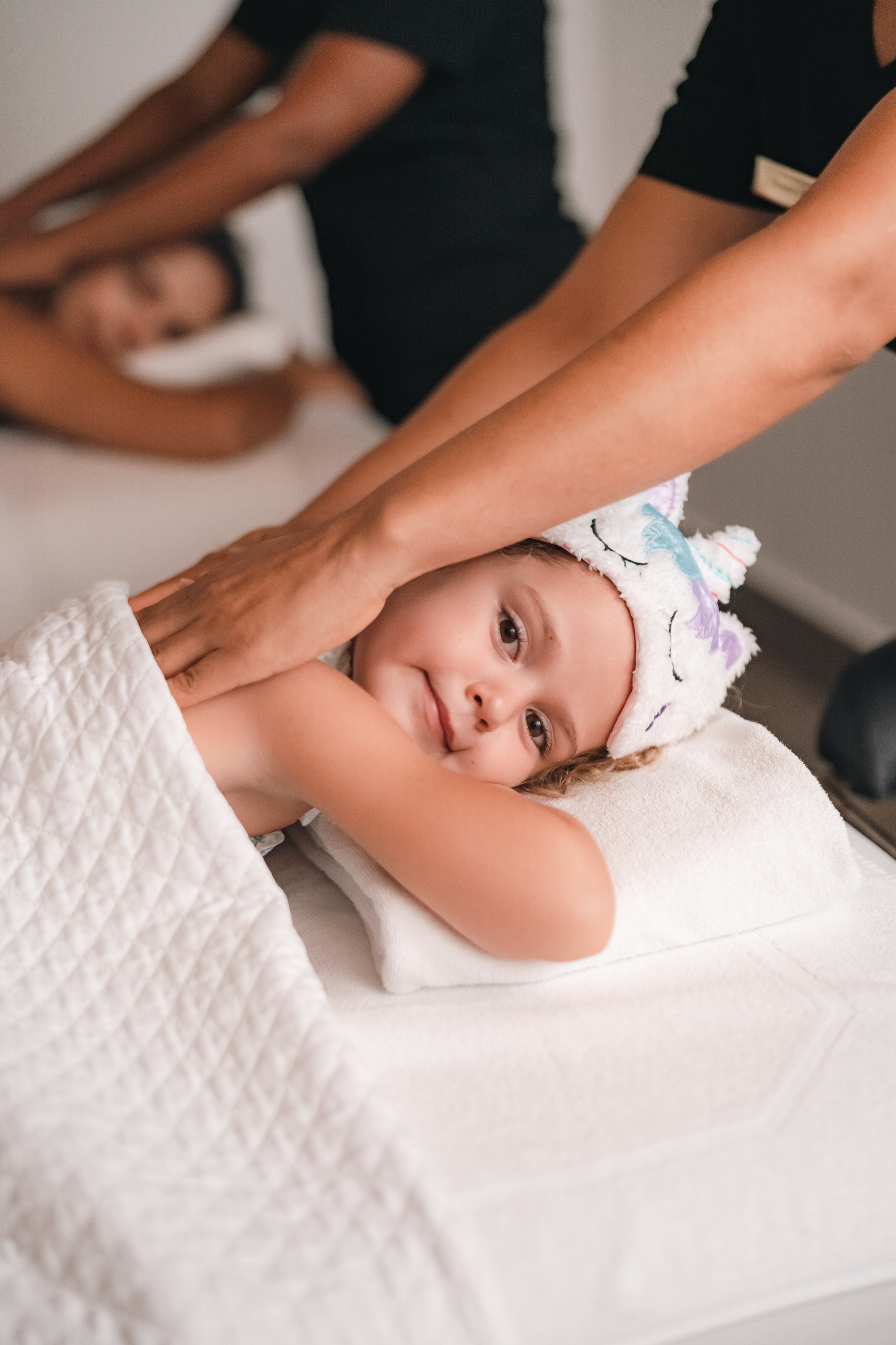 Young girl receiving a back massage at a spa, wearing a unicorn headband.