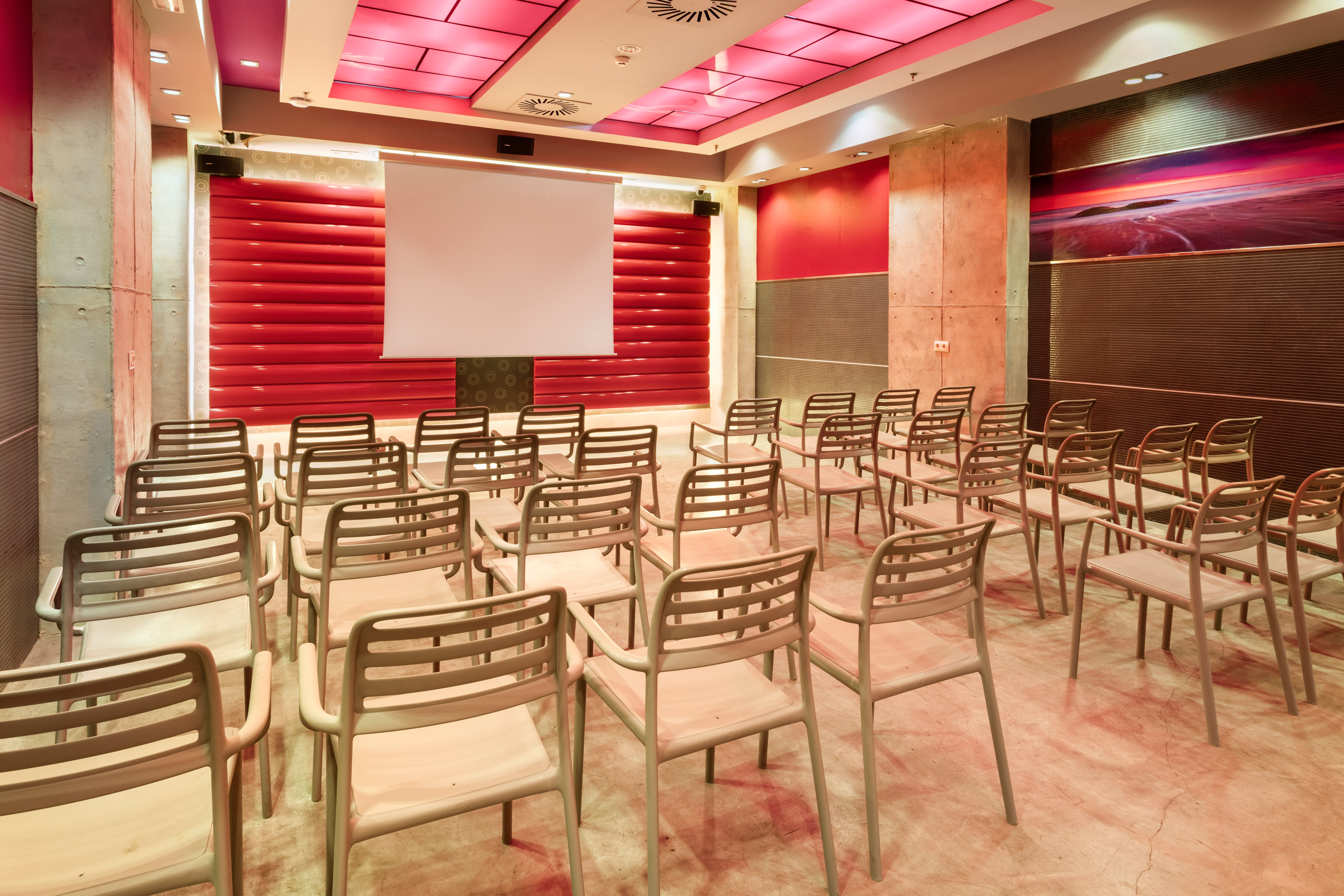 Empty modern conference room with red decor, seating, and projection screen.