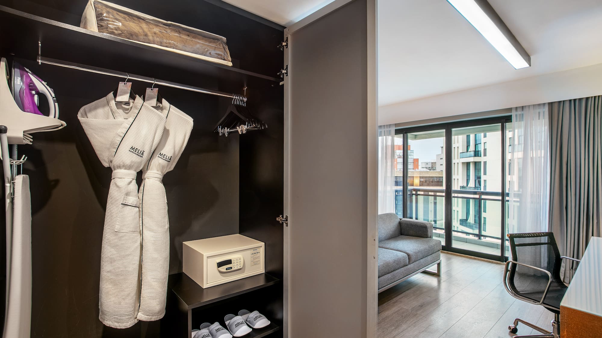 Hotel room wardrobe with bathrobes, safe, and iron, overlooking a living area. - Deluxe Queen Room com Varanda - Meliá Ibirapuera, São Paulo