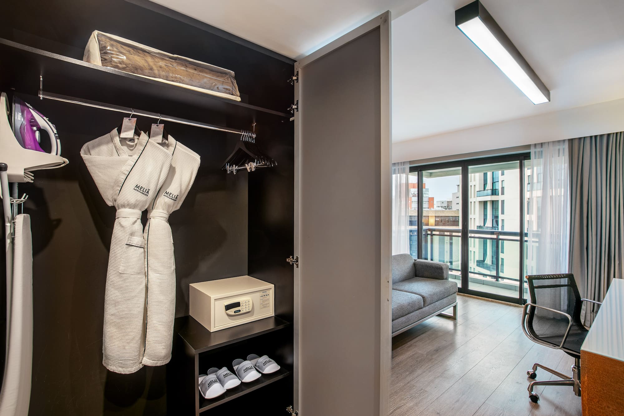 Hotel room wardrobe with bathrobes, safe, and iron, overlooking a living area. - Deluxe Queen Room com Varanda - Meliá Ibirapuera, São Paulo