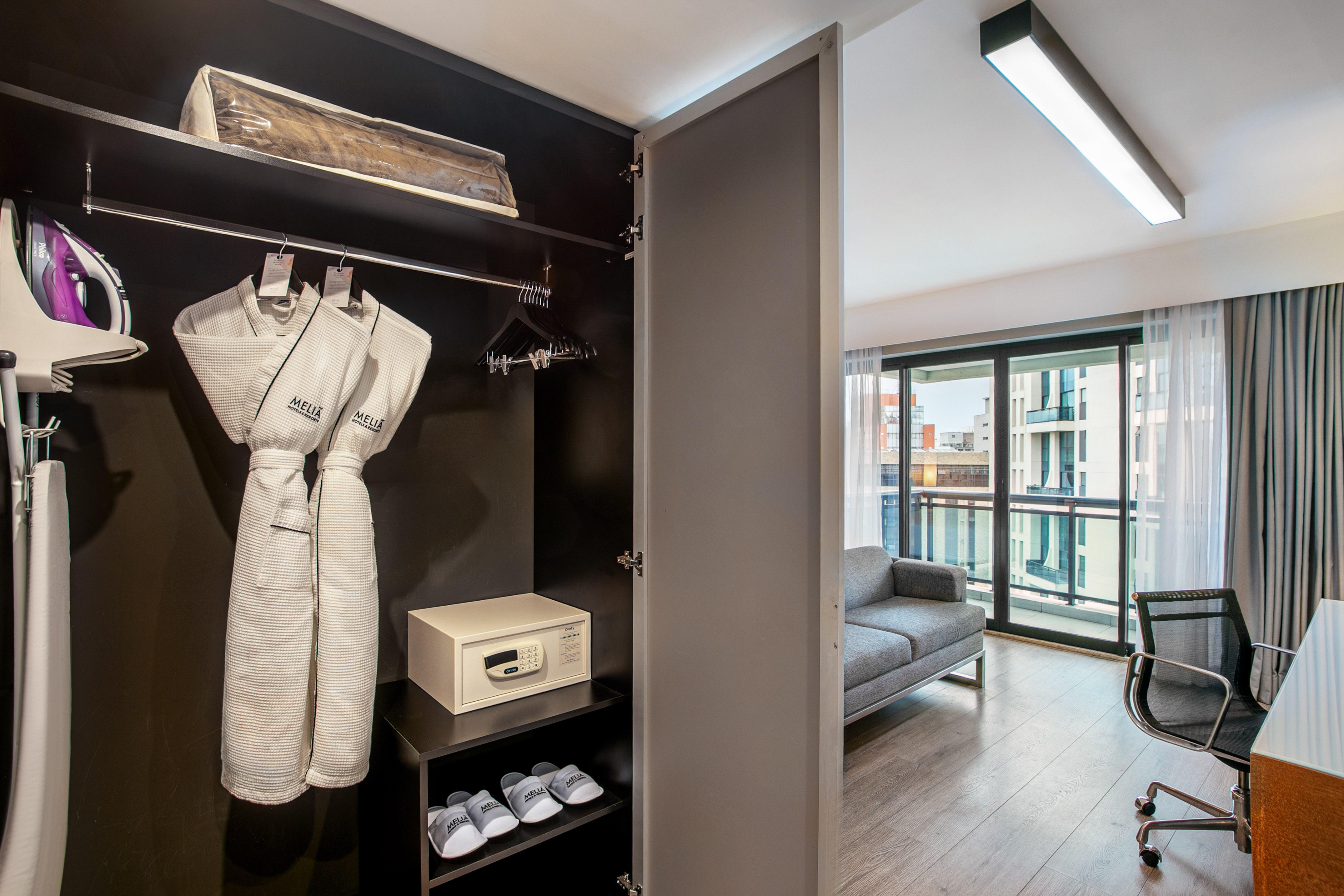 Hotel room wardrobe with bathrobes, safe, and iron, overlooking a living area. - Deluxe Queen Room com Varanda - Meliá Ibirapuera, São Paulo