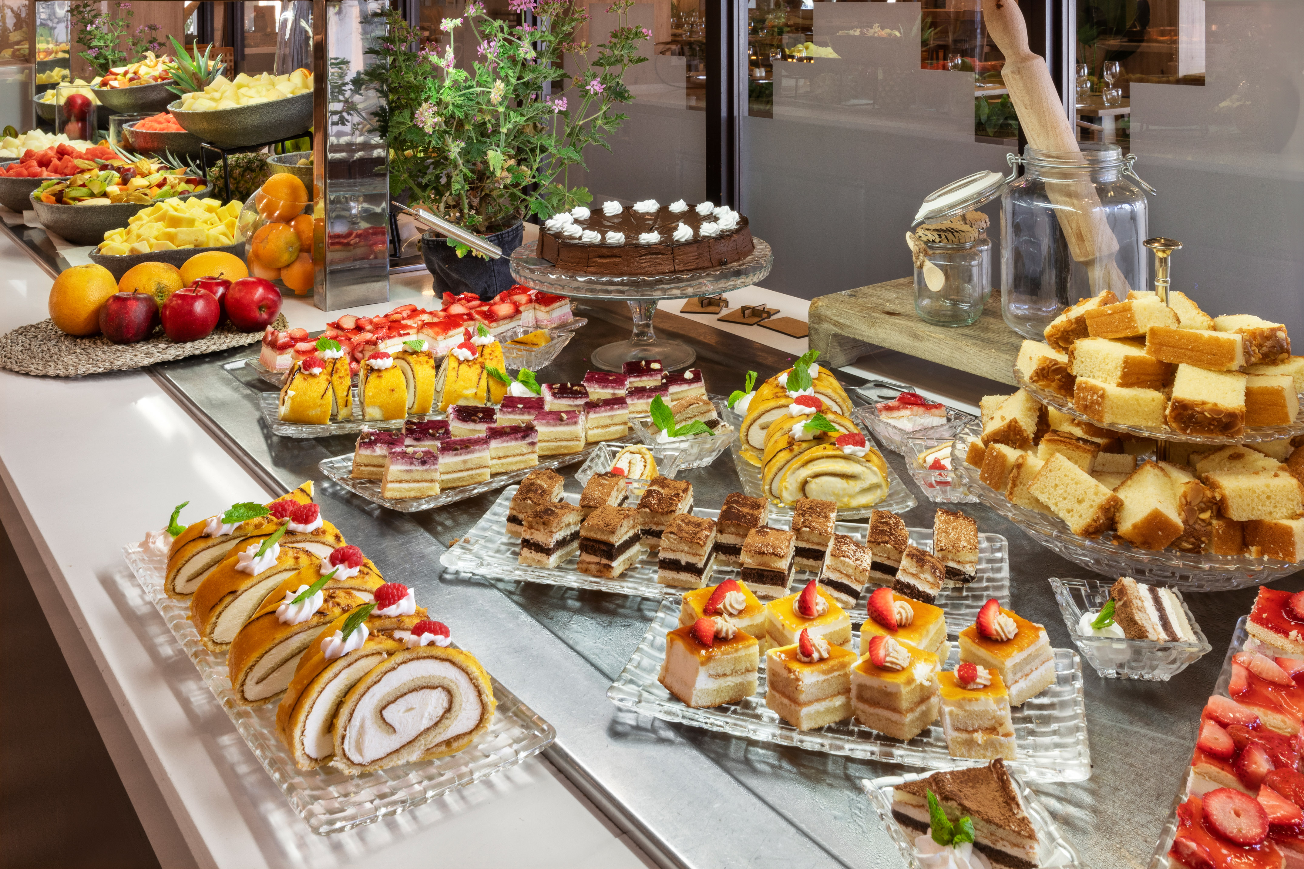 Hotel dessert buffet with assorted cakes, pastries, fruit rolls, and fresh fruit.