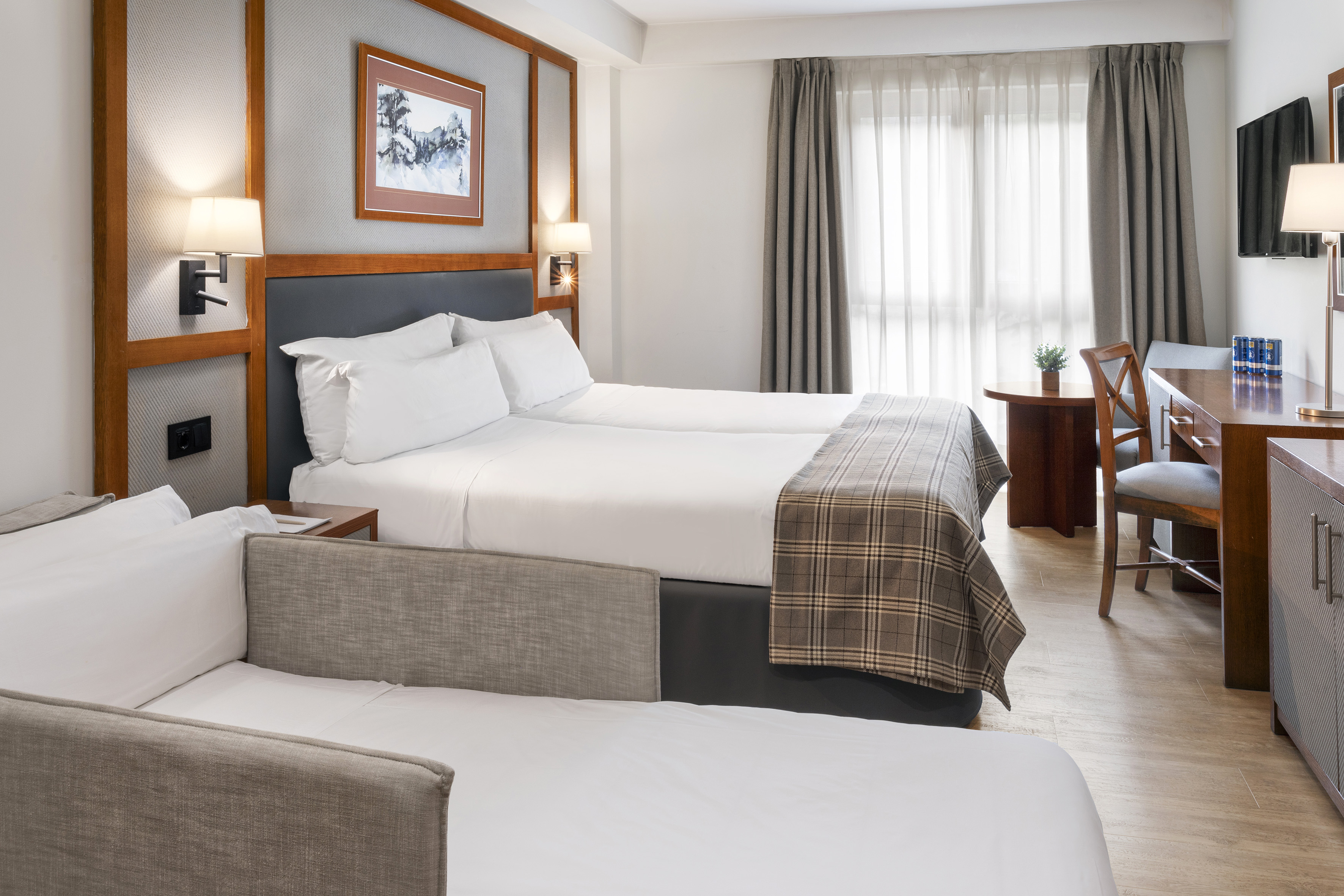 Hotel room with two twin beds, sofa bed, desk, TV, and window.