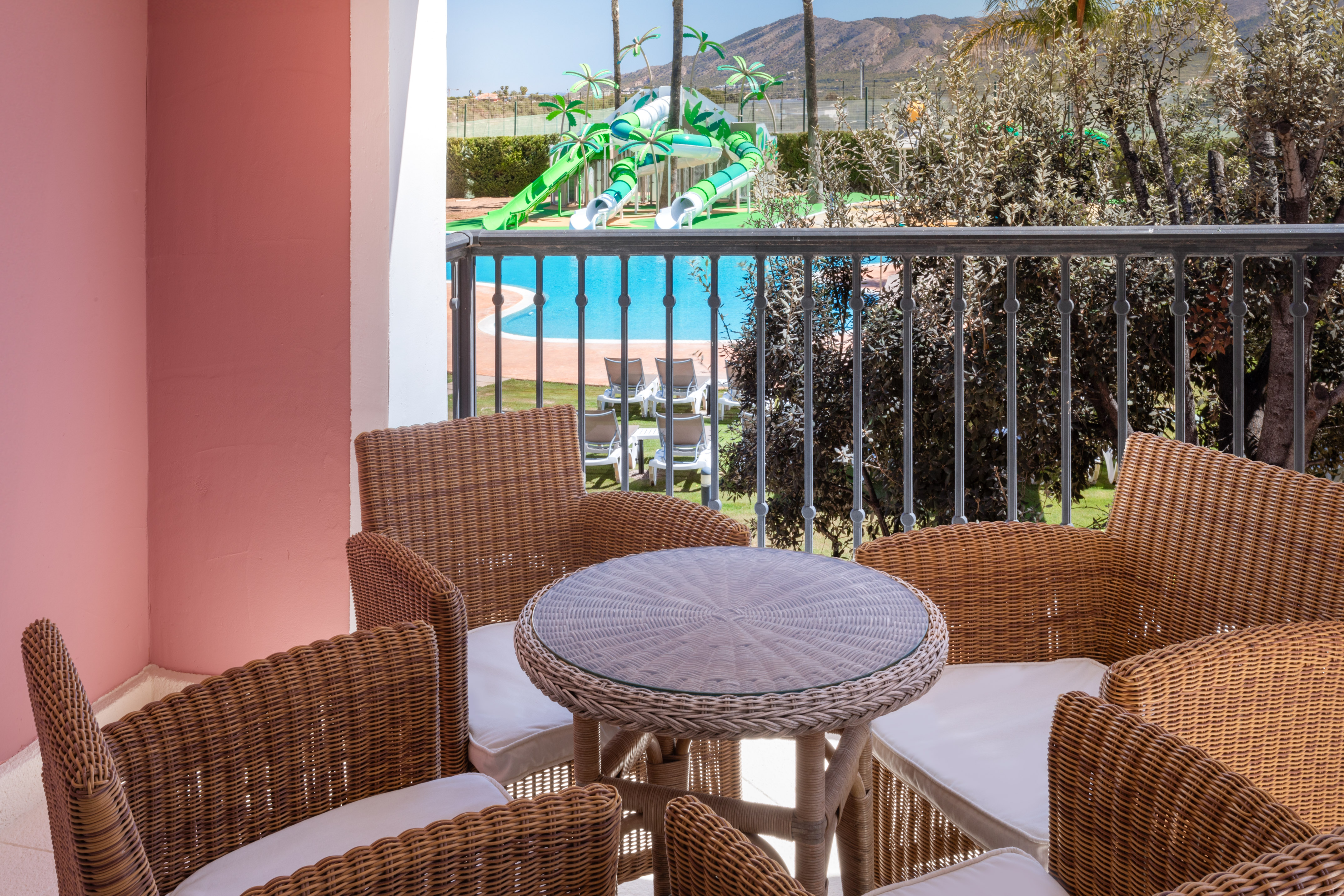 Balcony with wicker seating overlooking resort pool, water slides, and mountains.