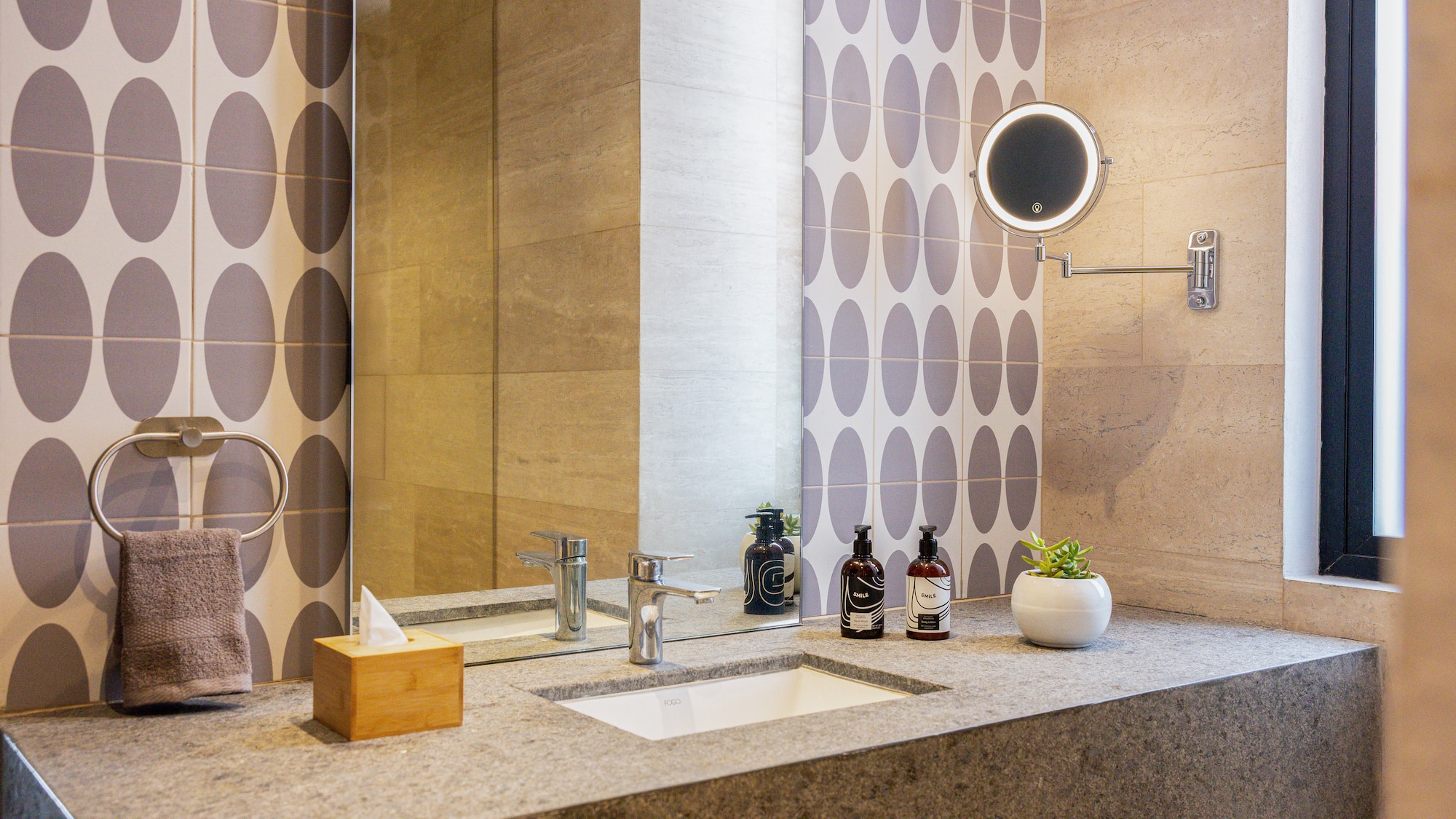 Baño moderno con lavabo de piedra, azulejos de patrón y espejo iluminado.