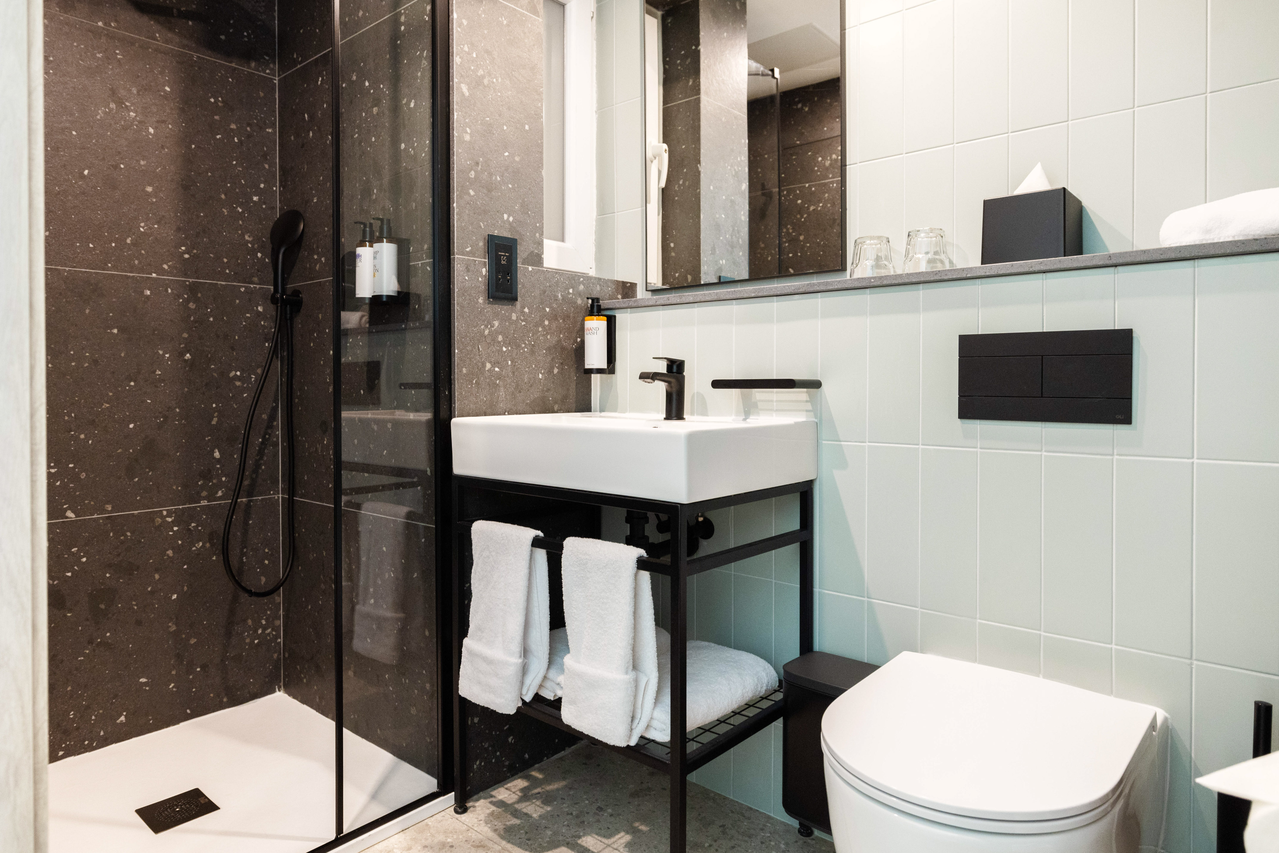 Contemporary bathroom: black framed shower, white sink, toilet, dark textured walls.