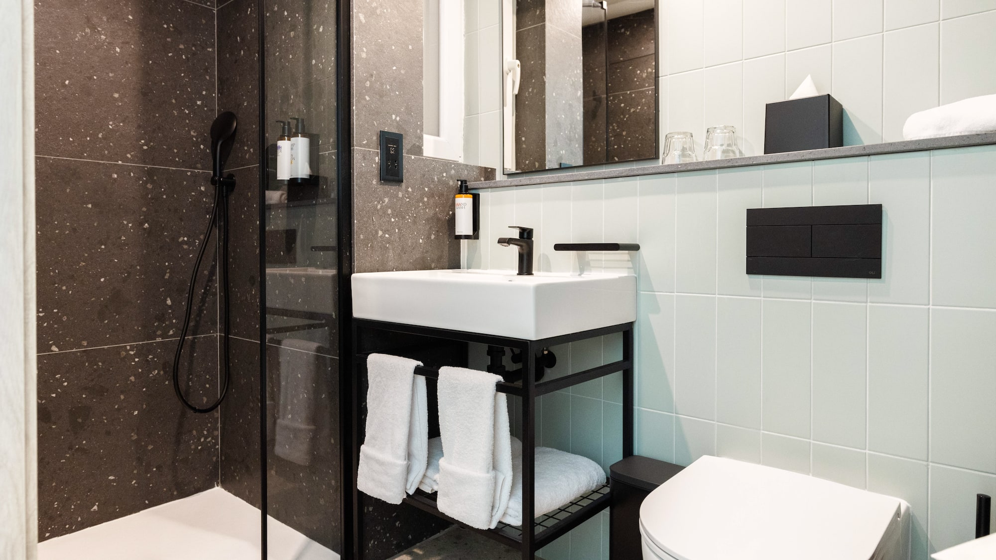 Contemporary bathroom: black framed shower, white sink, toilet, dark textured walls.