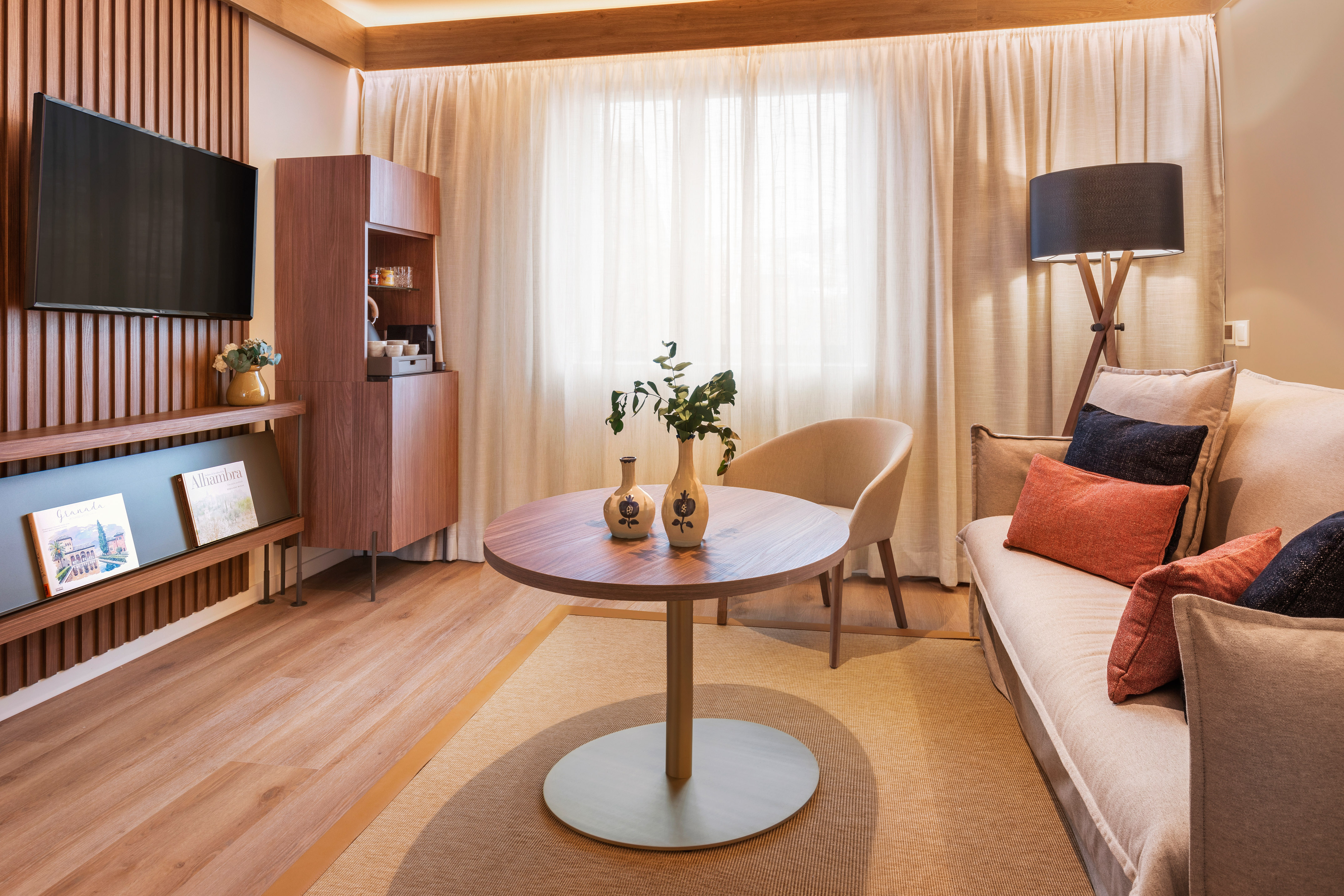 Cozy modern hotel room with sofa, TV, wood slatted wall, and bright window.