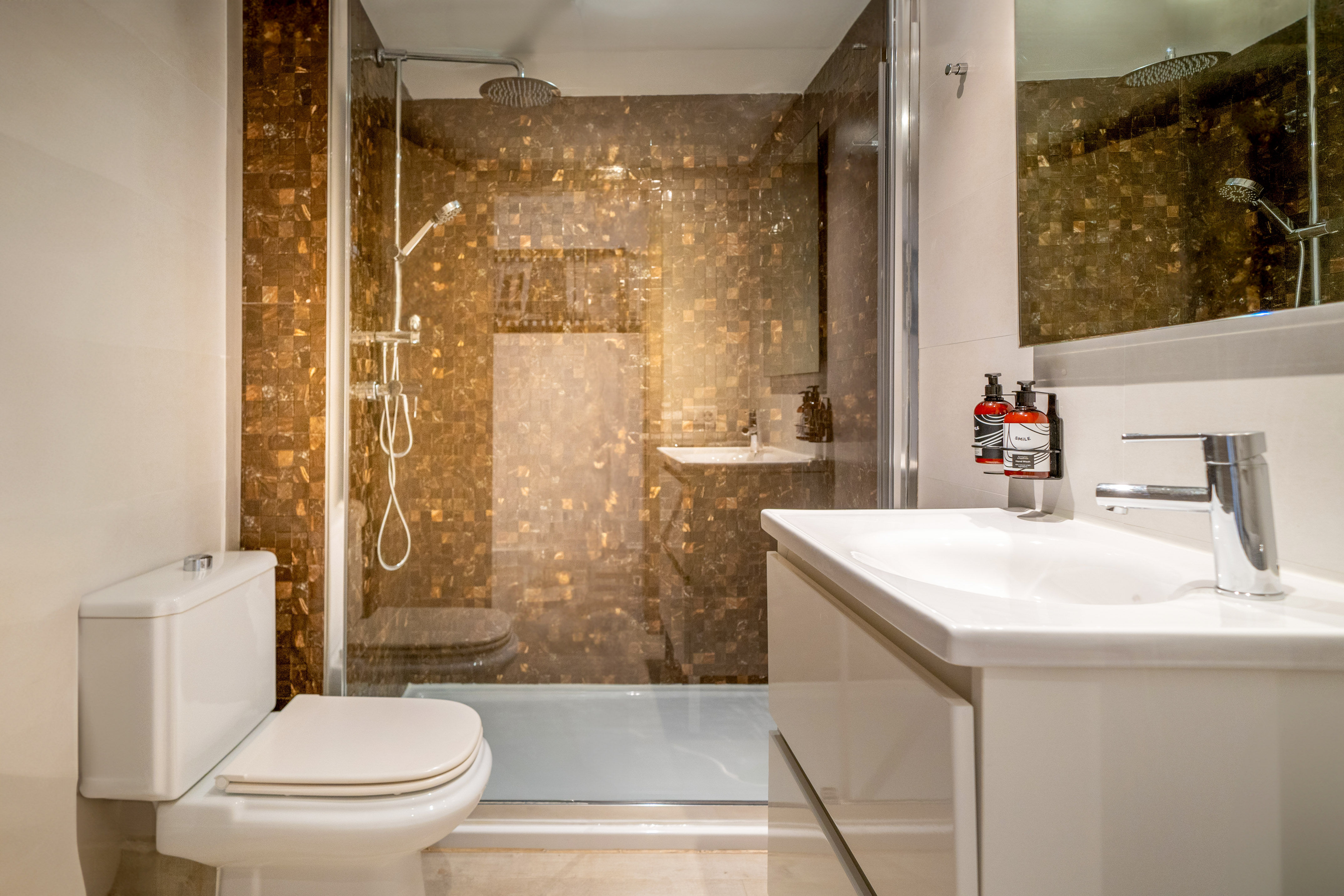 Modern bathroom: white toilet, vanity, and brown mosaic walk-in shower.