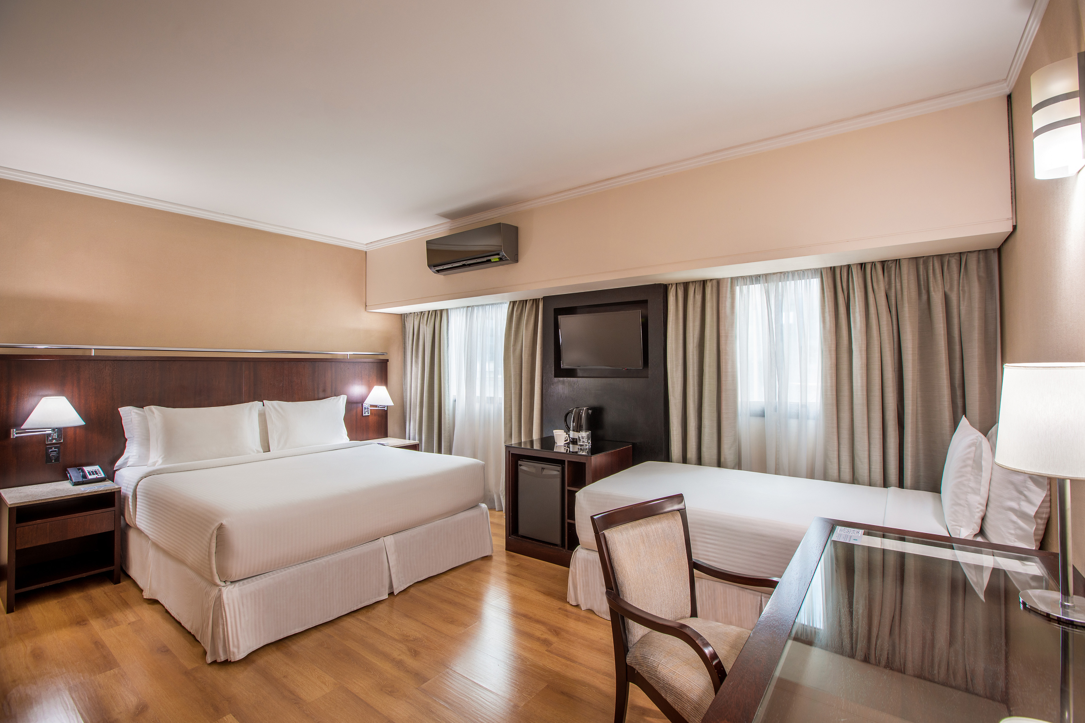 Hotel guest room with a large bed, single bed, TV, desk, and minibar.