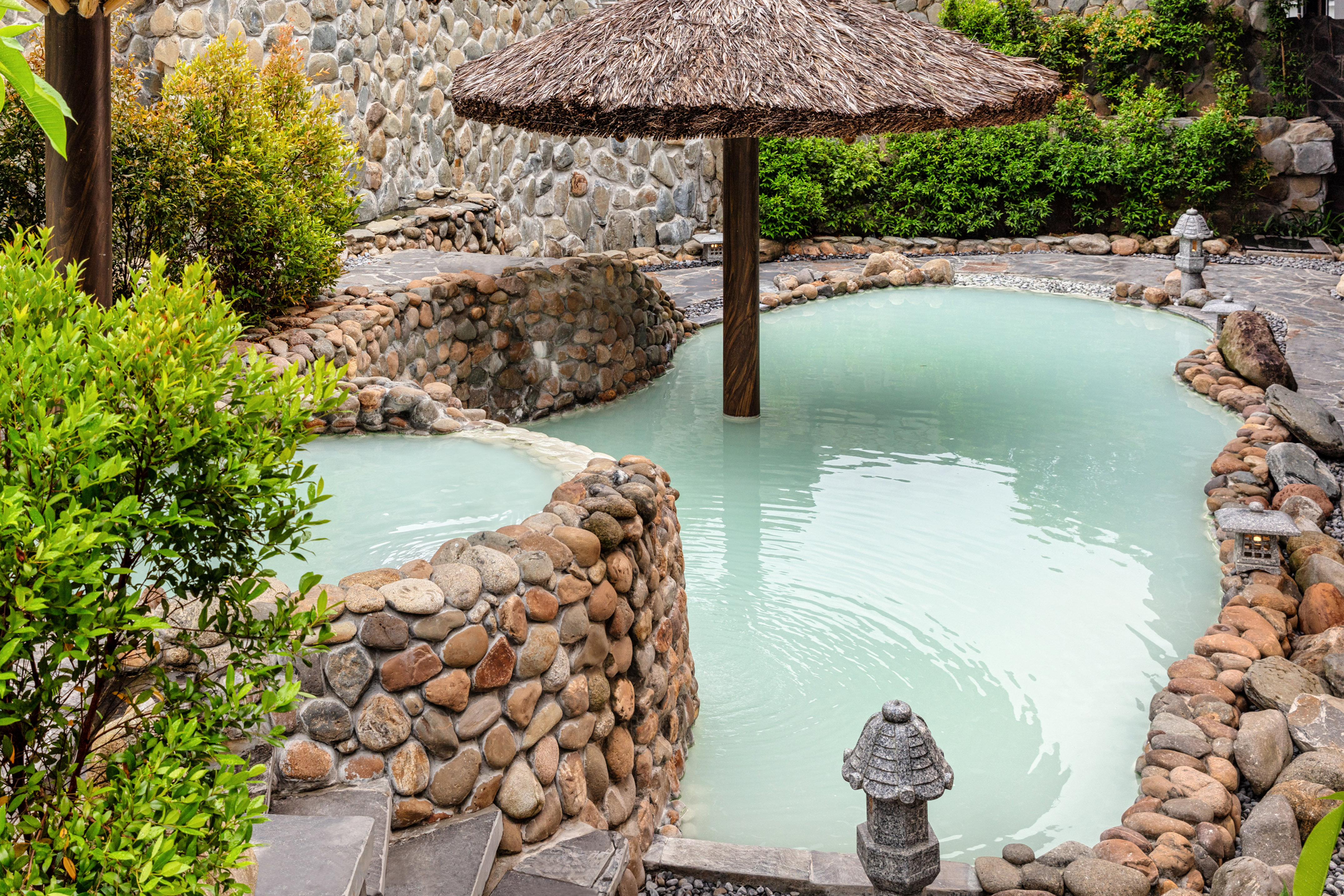 Tiered stone hot springs with milky green water and thatched umbrella.