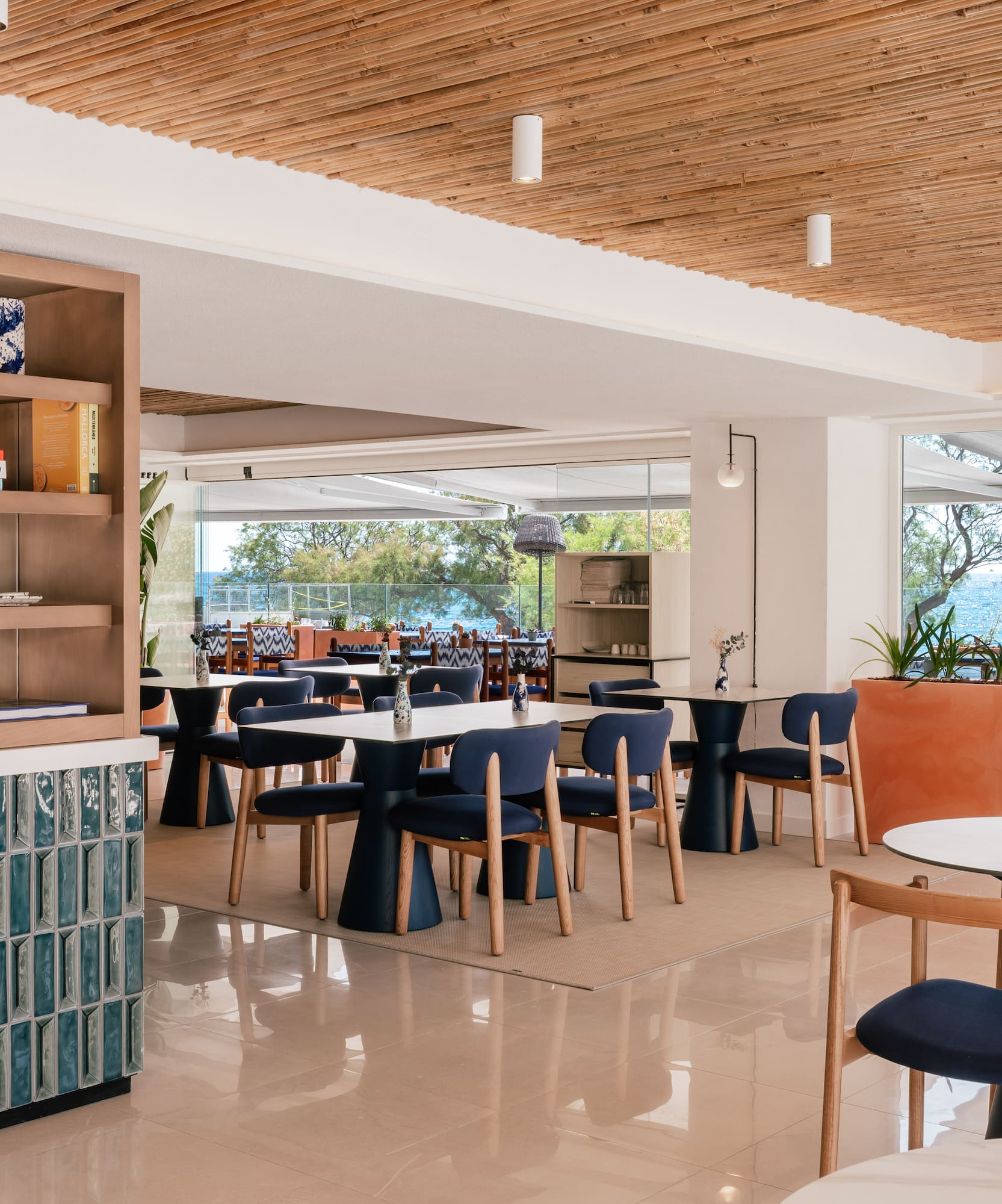 Modern Mediterranean restaurant with ocean view, blue seating, bamboo ceiling.