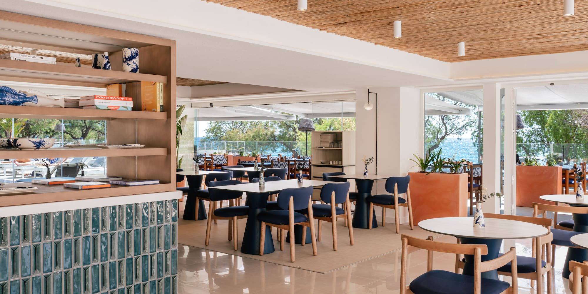 Modern Mediterranean restaurant with ocean view, blue seating, bamboo ceiling.