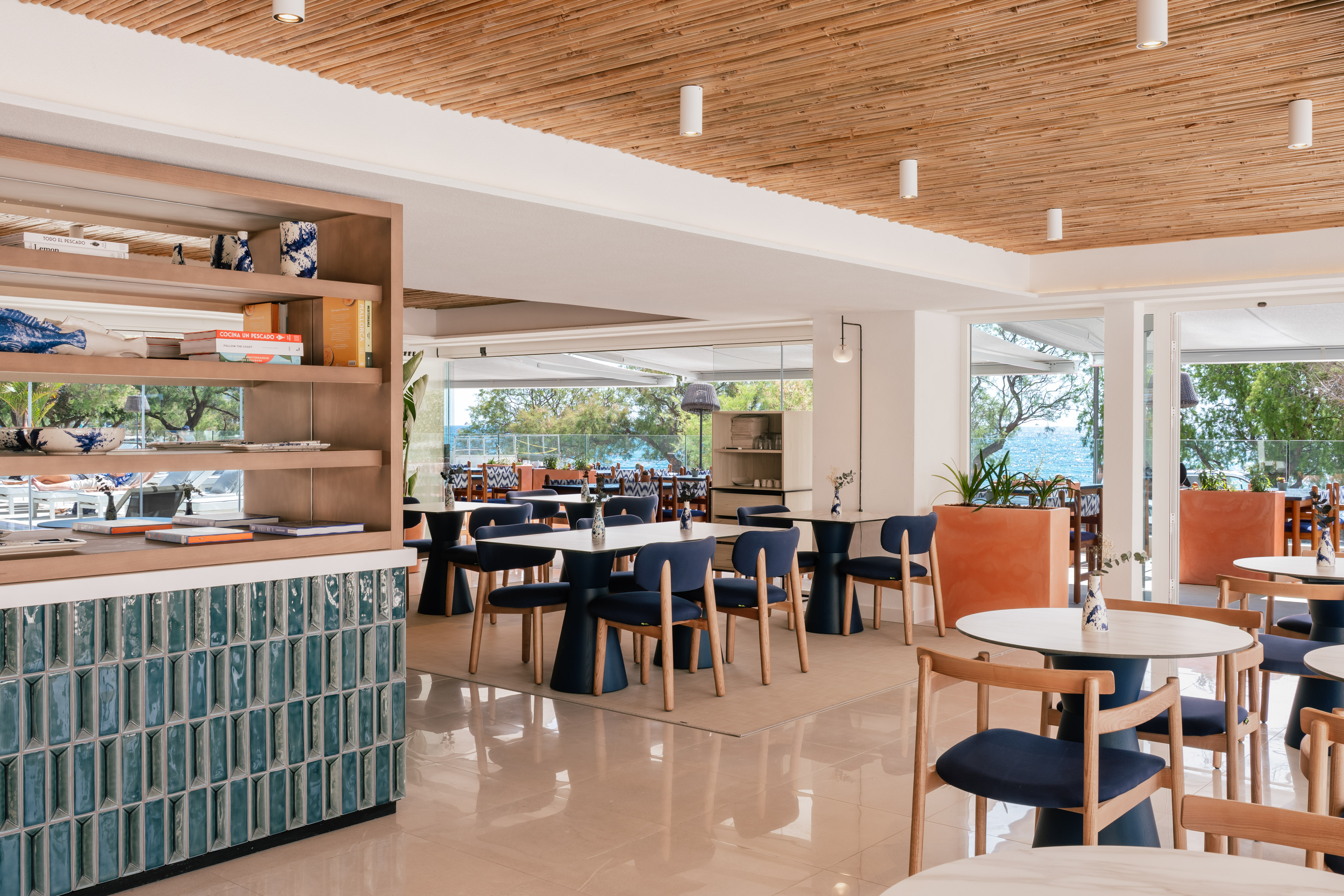 Modern Mediterranean restaurant with ocean view, blue seating, bamboo ceiling.
