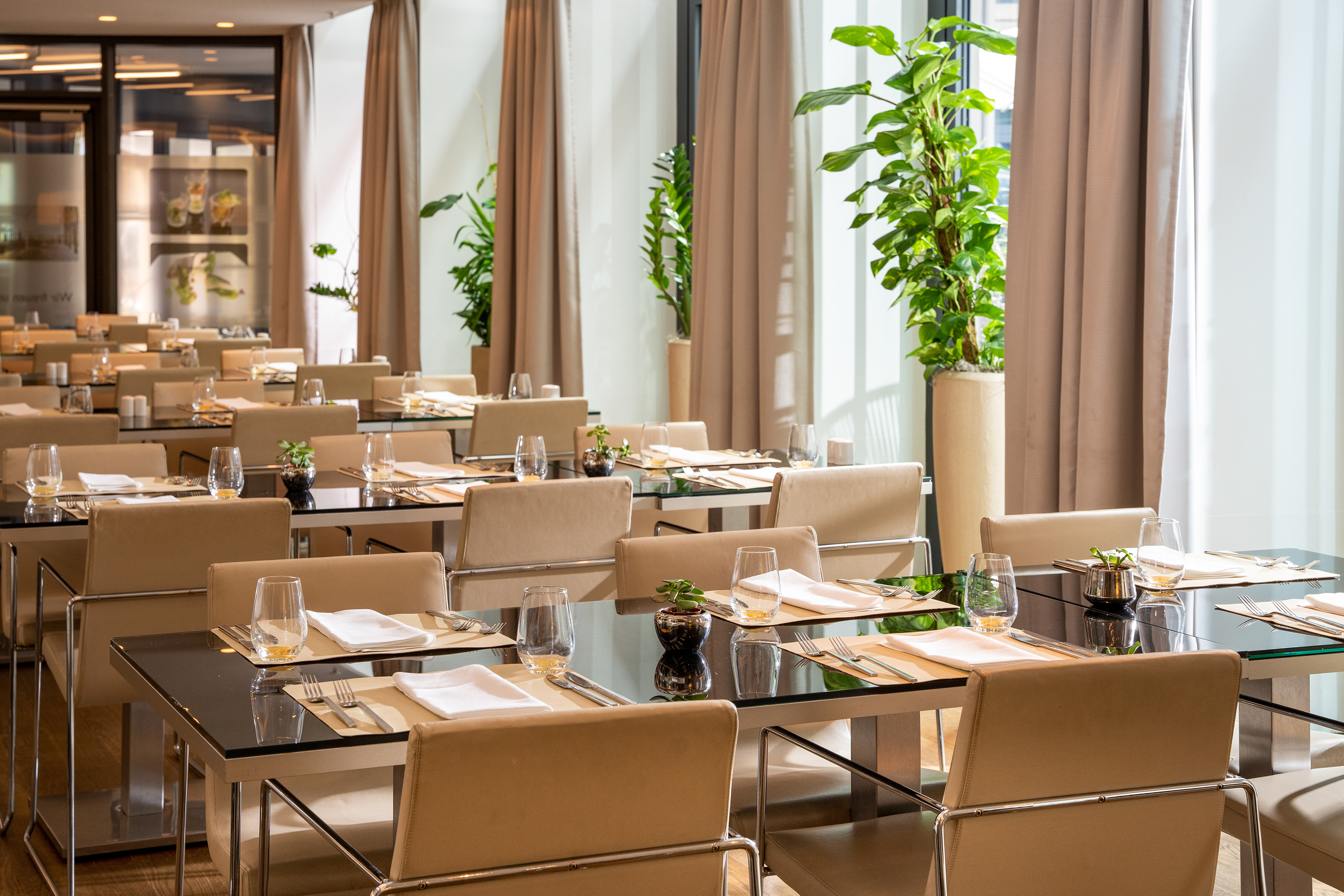 Modern restaurant dining room with set tables, beige chairs, and green plants. - Restaurant VEN - Innside Dresda, Dresda