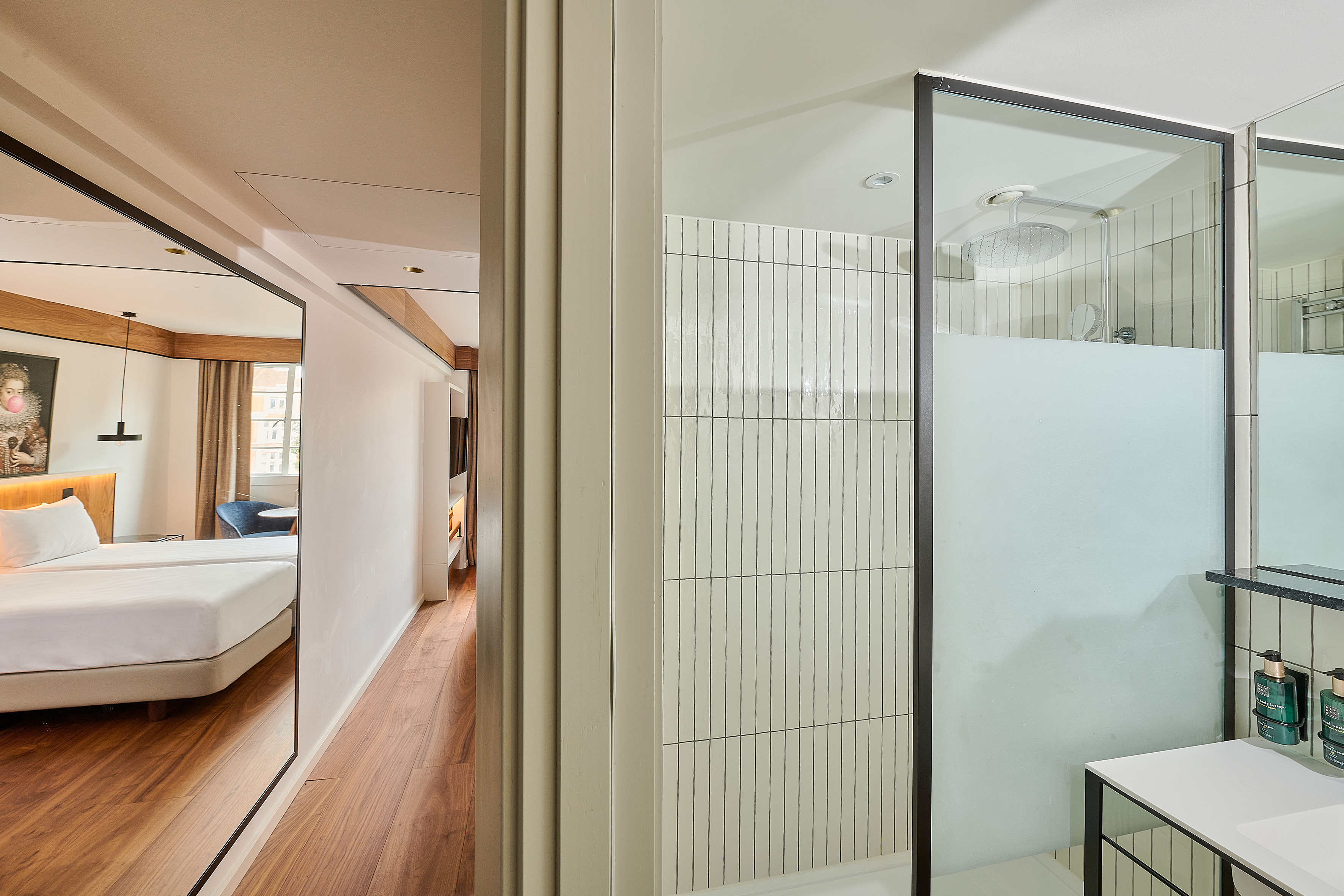 Modern hotel room interior with bedroom reflected in mirror and glass shower.