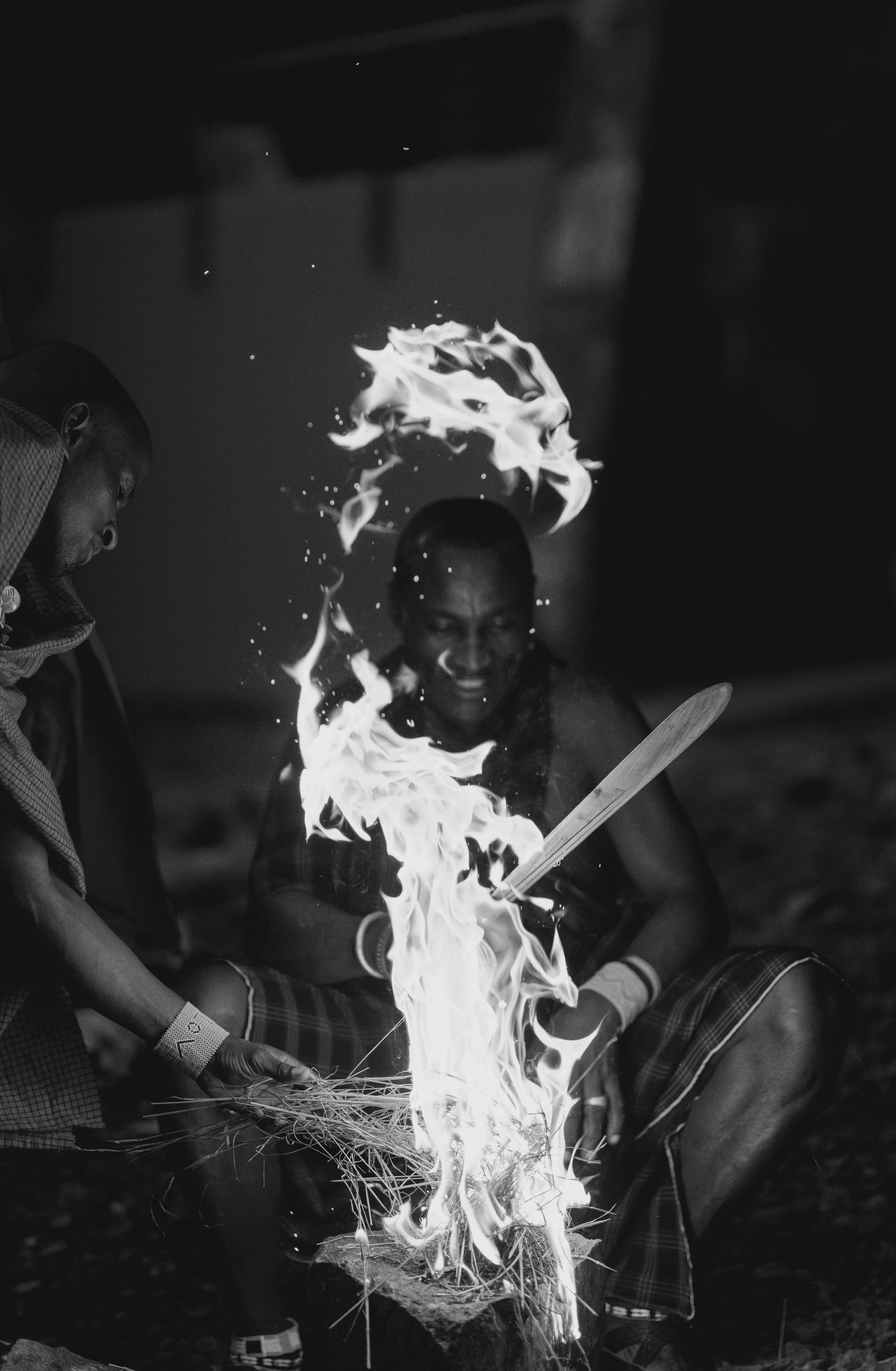 Traditional fire-making: two men ignite kindling, flames and sparks rise.
