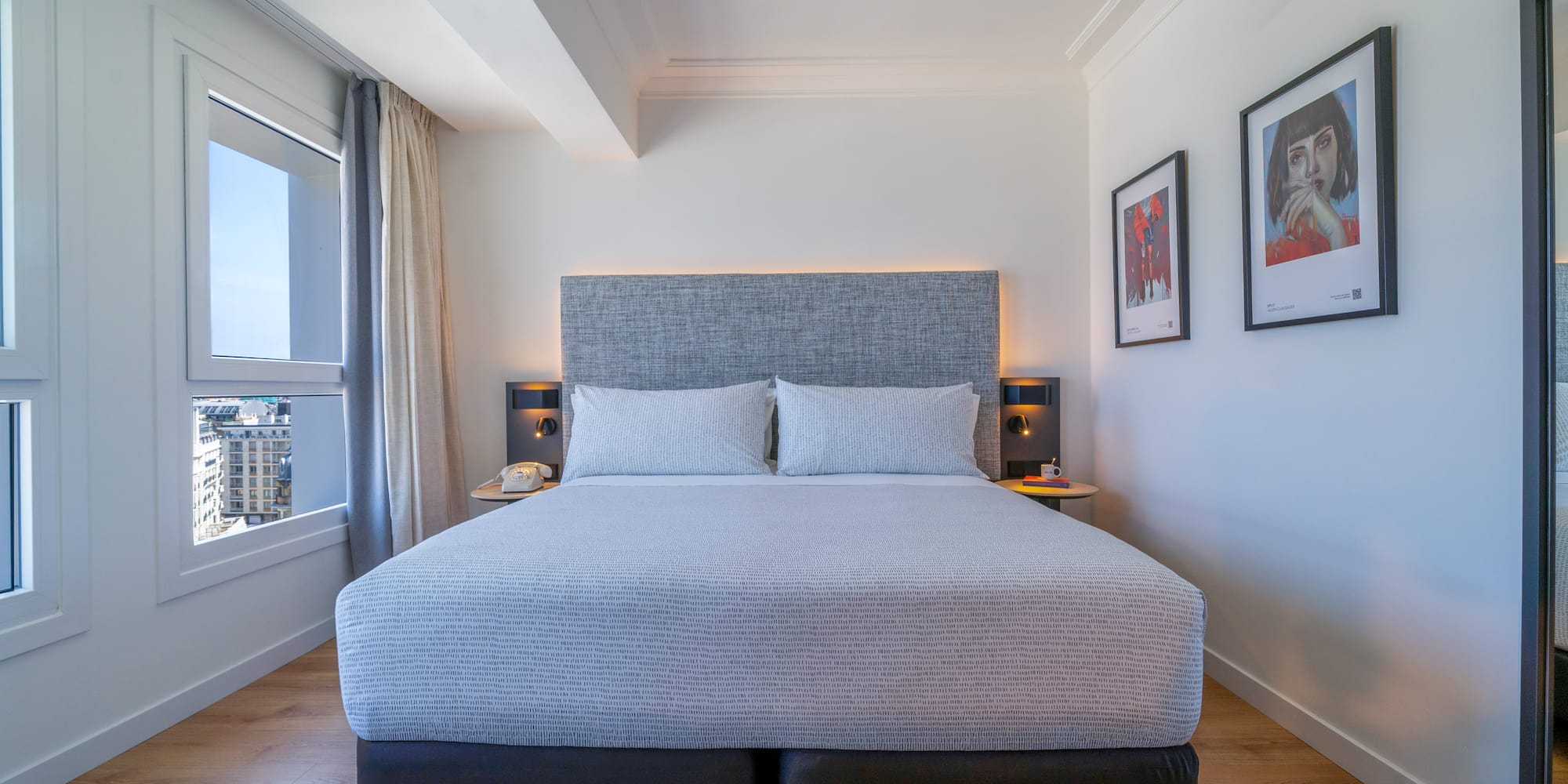 Habitación de hotel moderna con cama king-size, vistas urbanas y suelo de madera.