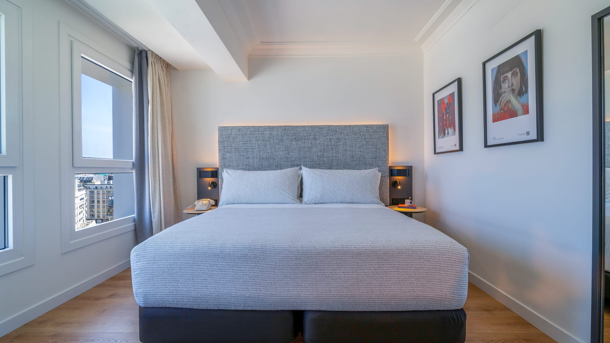 Habitación de hotel moderna con cama king-size, vistas urbanas y suelo de madera.