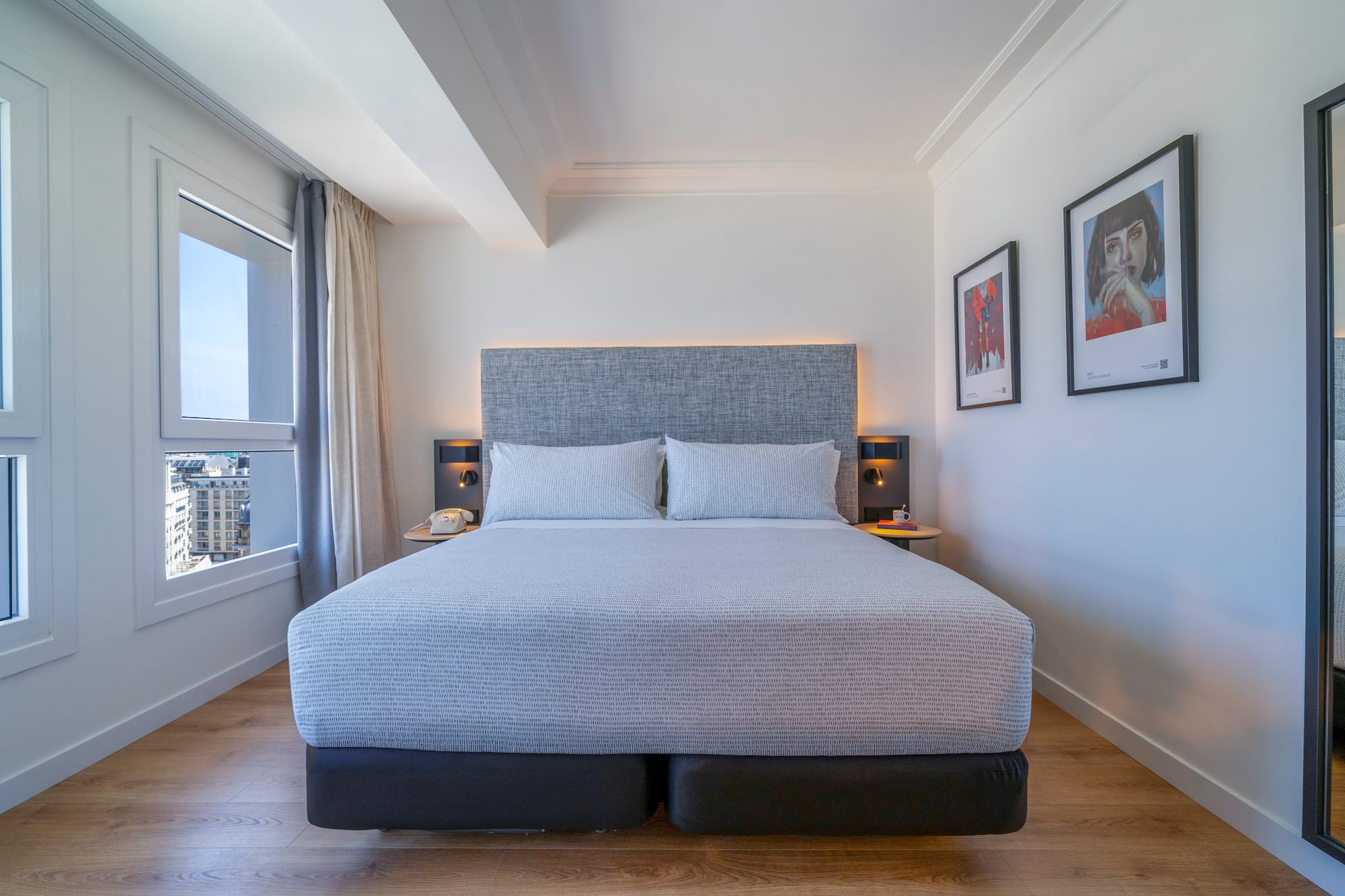 Habitación de hotel moderna con cama king-size, vistas urbanas y suelo de madera.