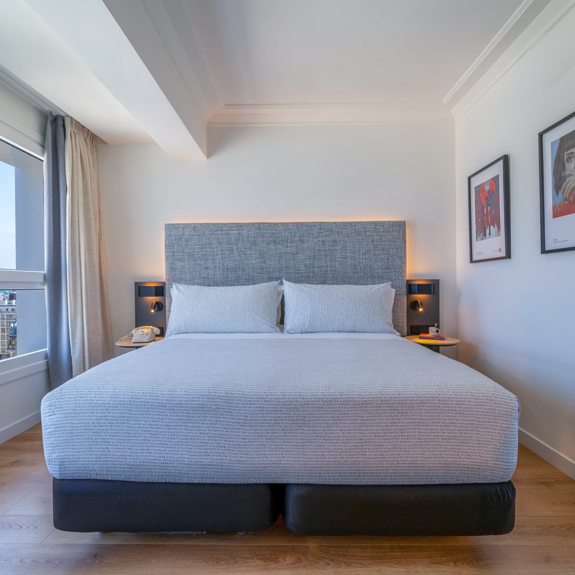 Habitación de hotel moderna con cama king-size, vistas urbanas y suelo de madera.