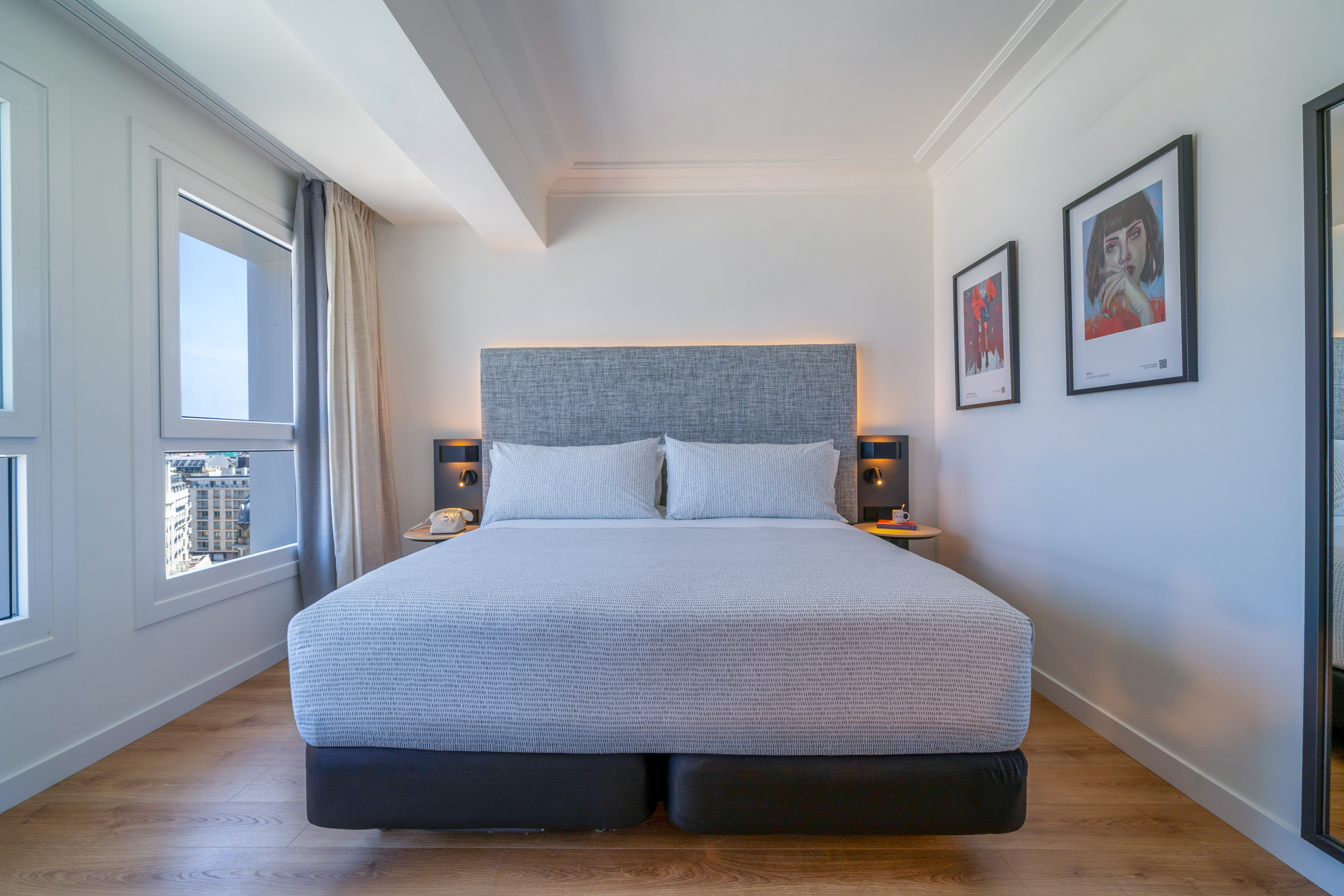 Habitación de hotel moderna con cama king-size, vistas urbanas y suelo de madera.