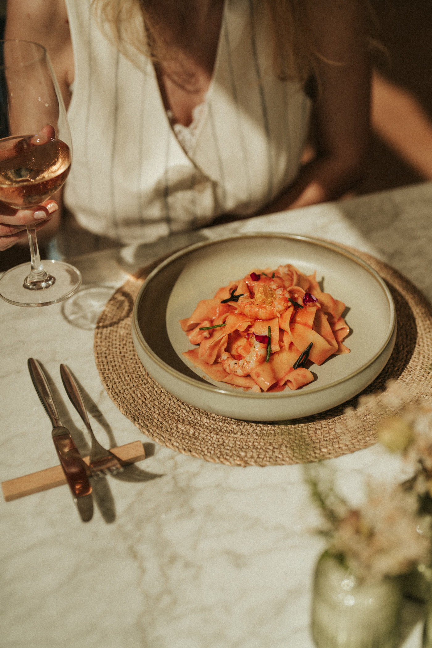 Shrimp pappardelle pasta with rosé wine at a sunlit dining table.