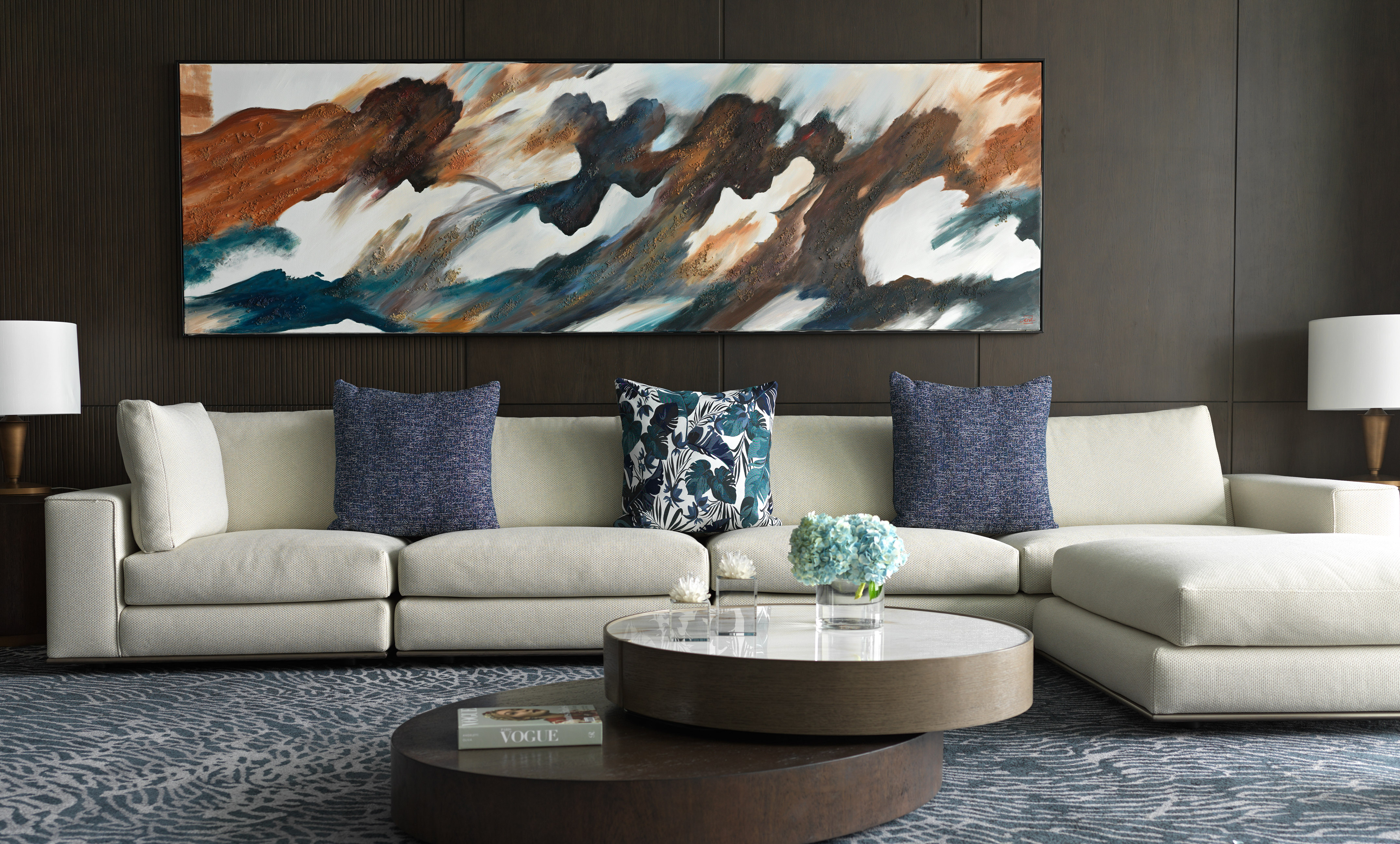 Modern living room with cream sectional sofa, abstract art, and blue rug.