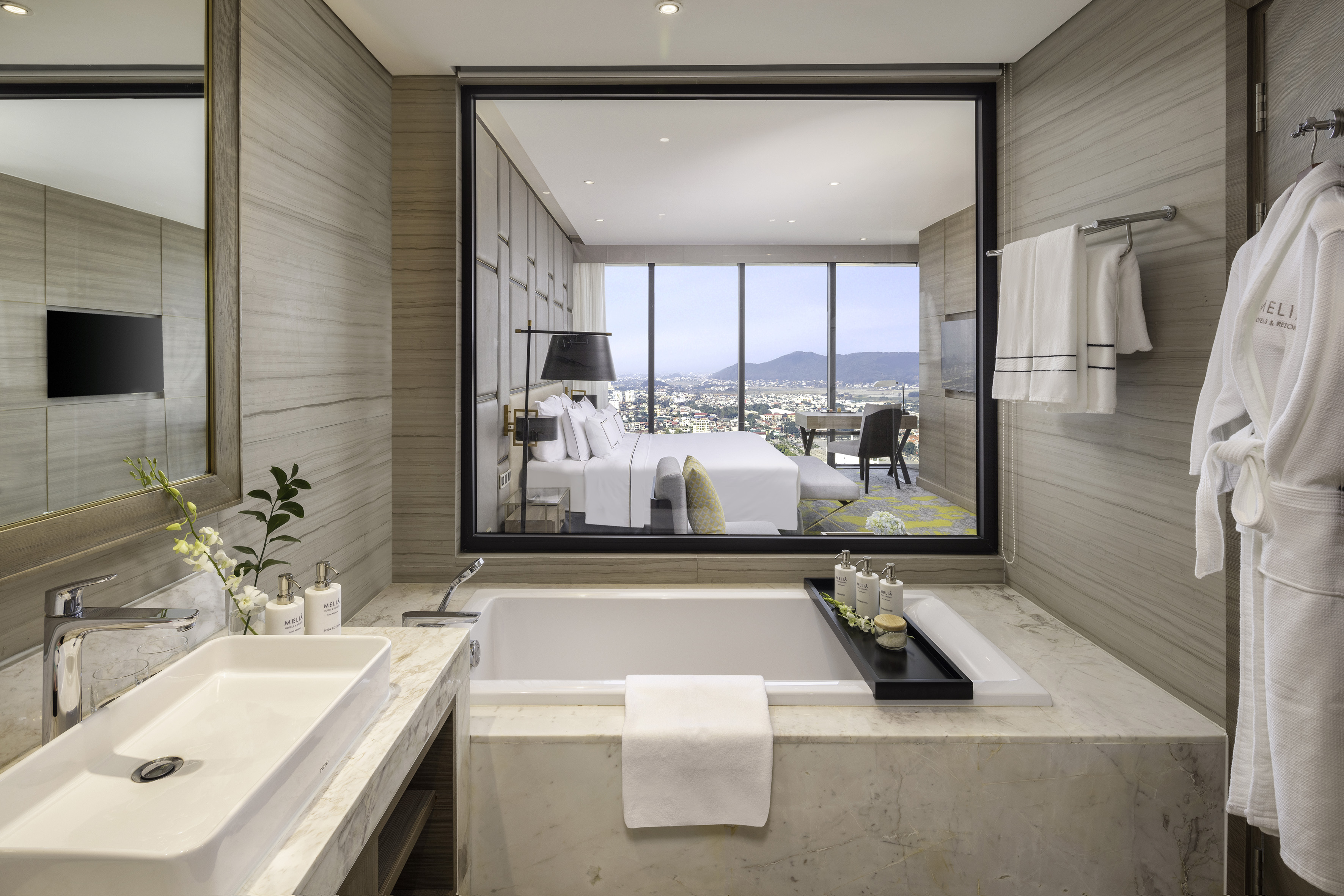 Modern hotel bathroom with bathtub and city view from adjoining bedroom.