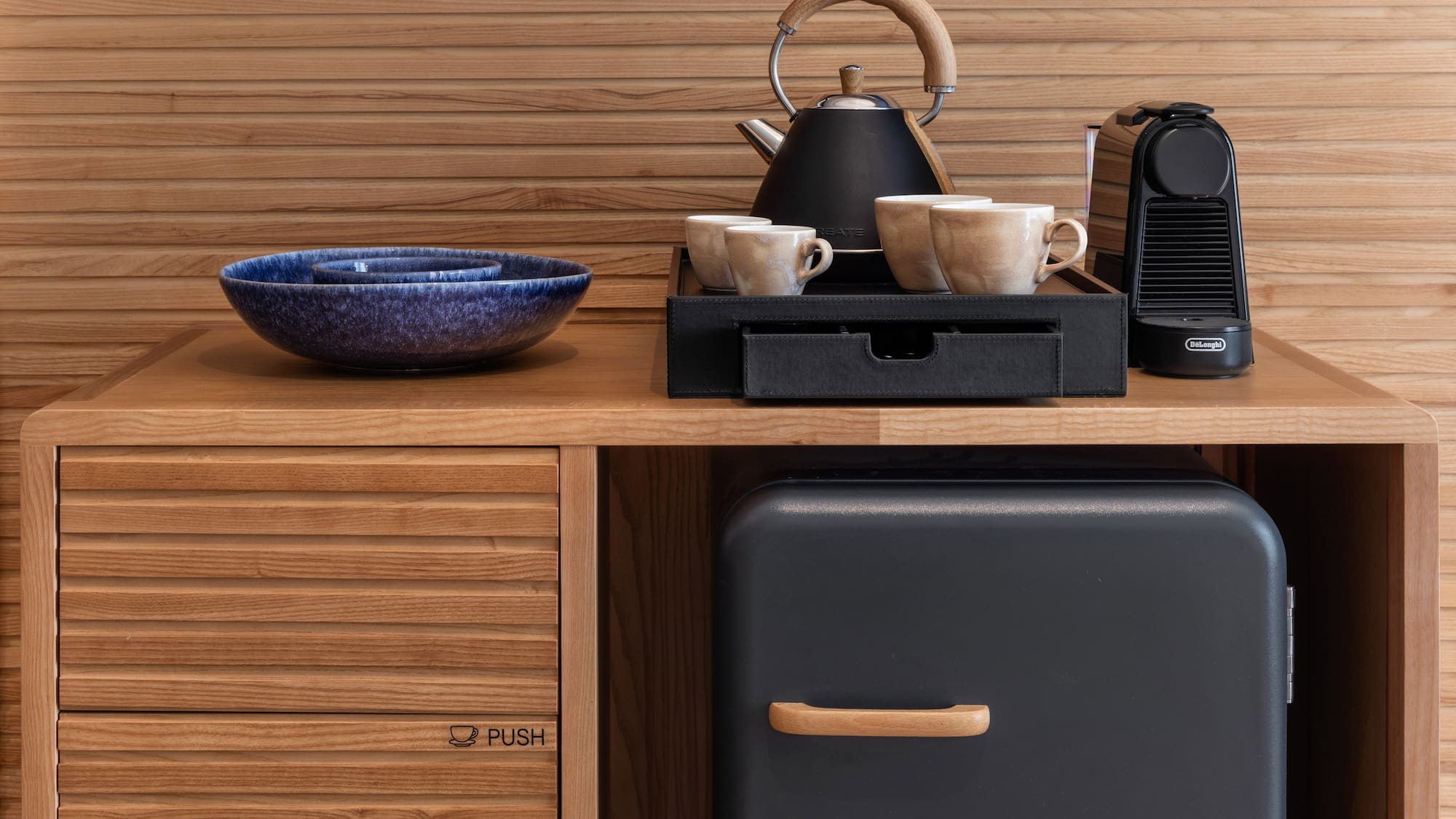 Minibar, cafetera Nespresso y tetera en mueble de madera de hotel.