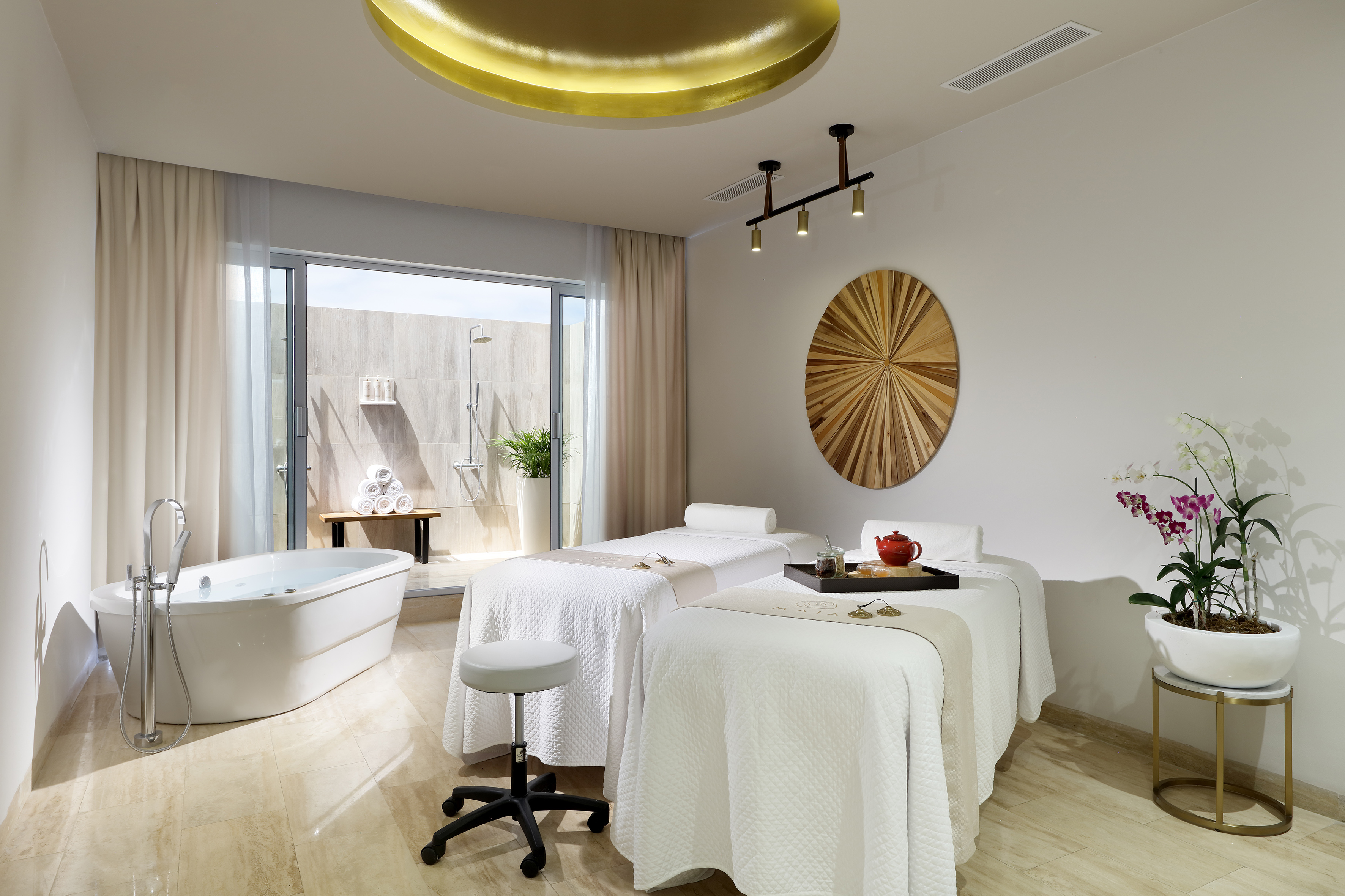 Bright spa room with dual massage beds, freestanding tub, and outdoor shower.