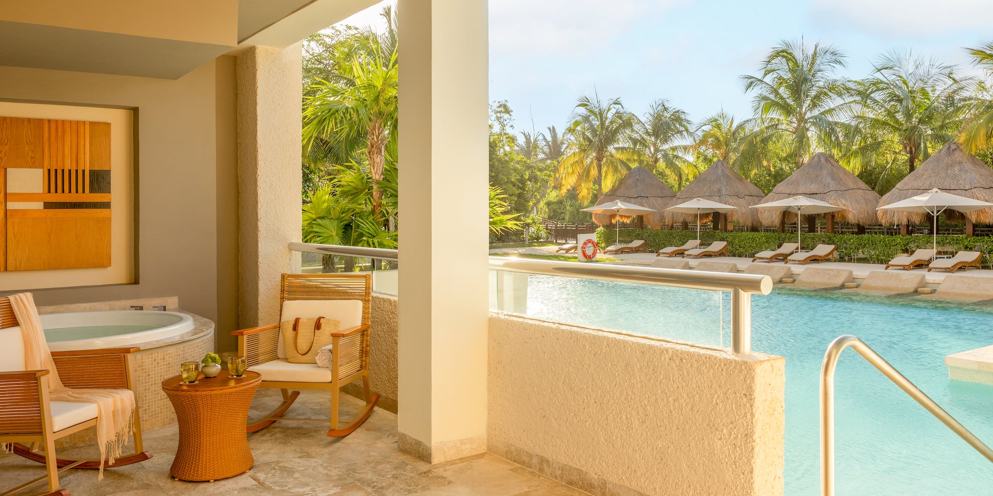 Hotel suite balcony with hot tub overlooking tropical resort pool and cabanas.