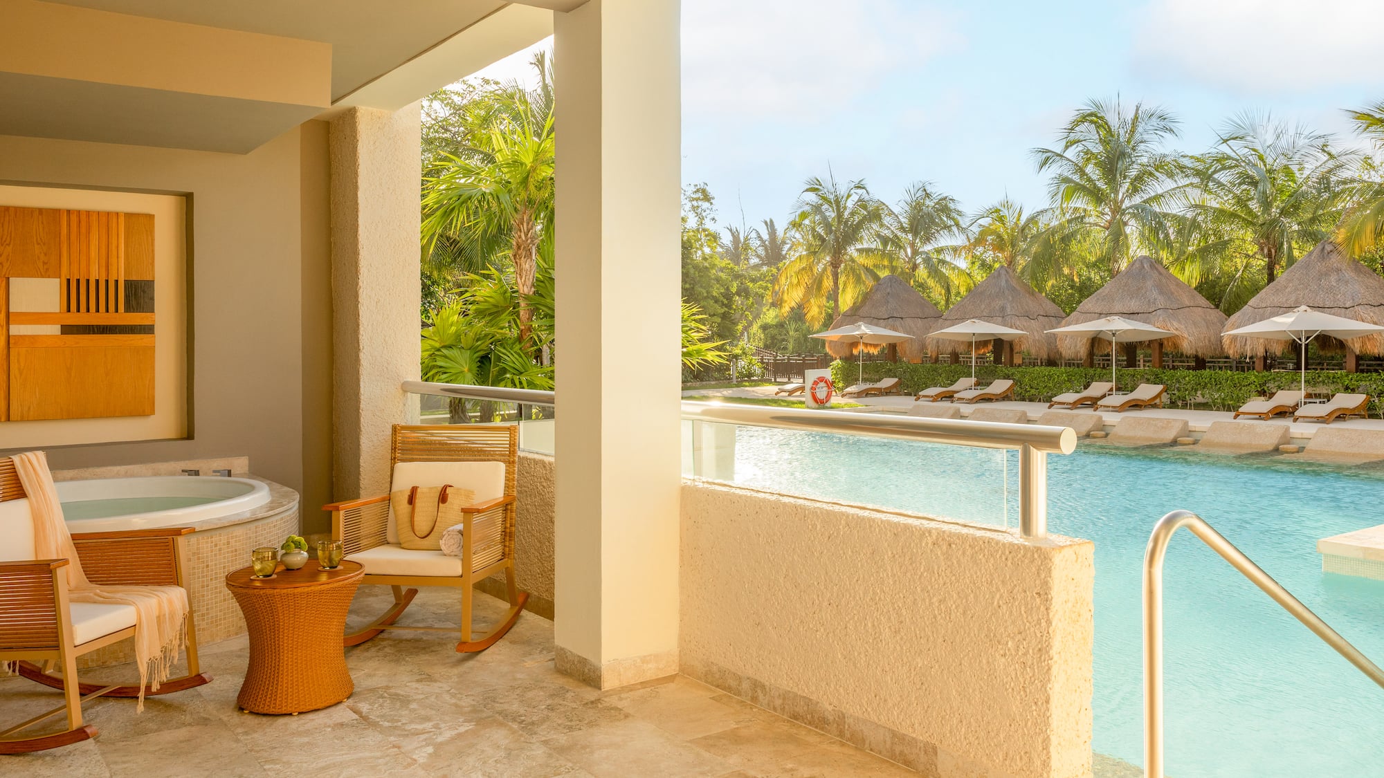 Hotel suite balcony with hot tub overlooking tropical resort pool and cabanas.